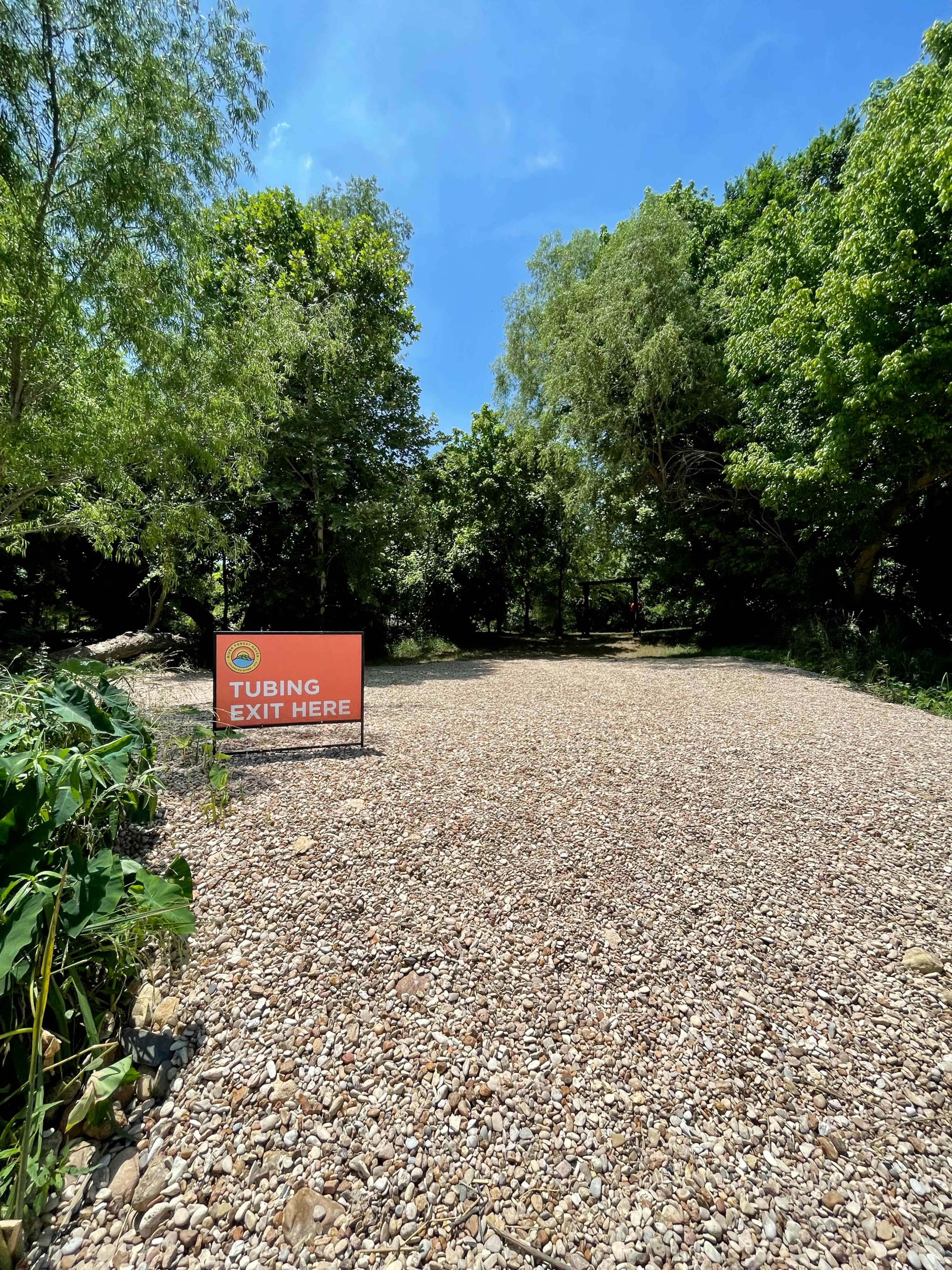 A sign instructing tubers to exit is positioned on a gravel pathway surrounded by trees.