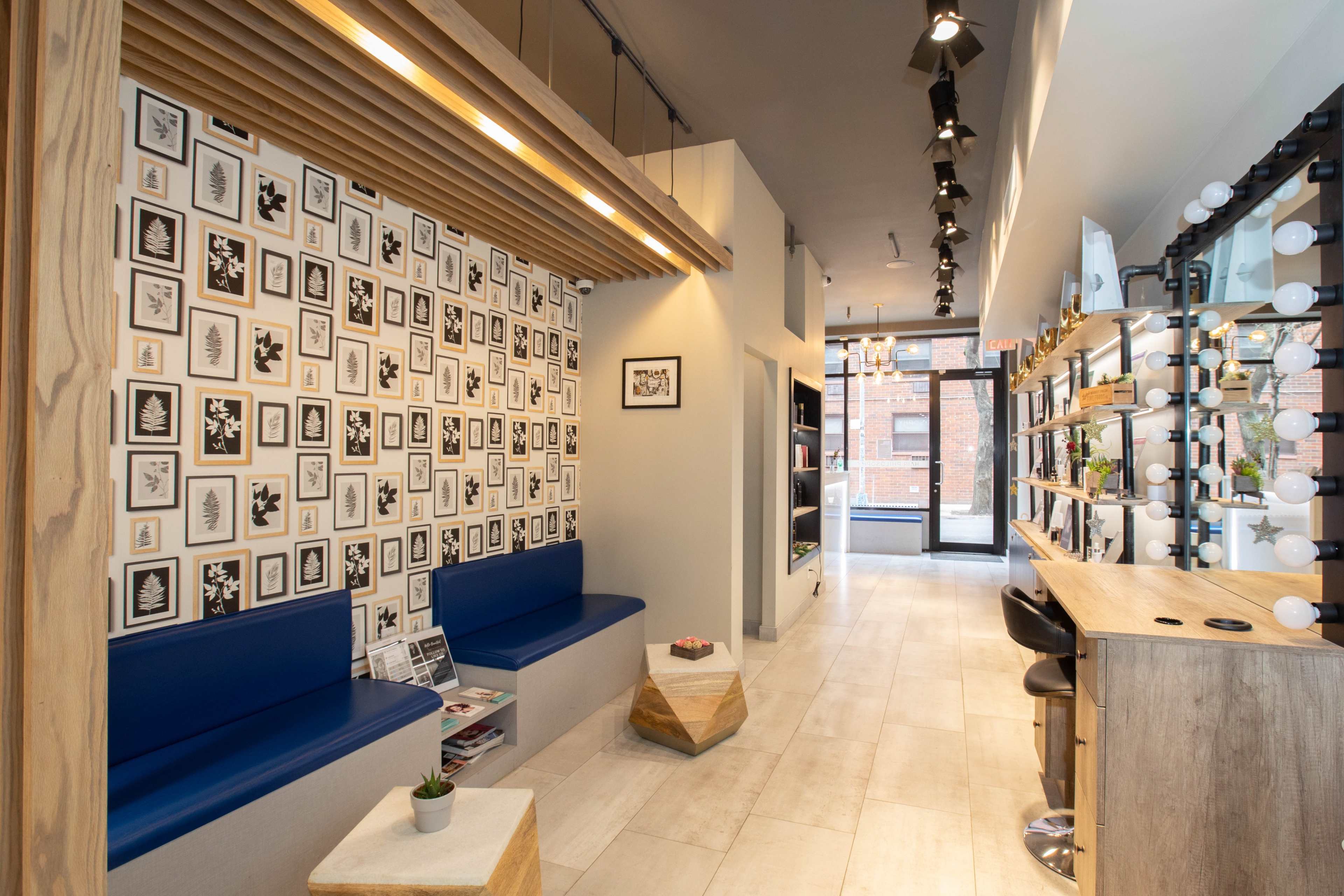 A modern interior space with a patterned wall of framed artworks, blue seating, and a sleek bar area lined with lights.