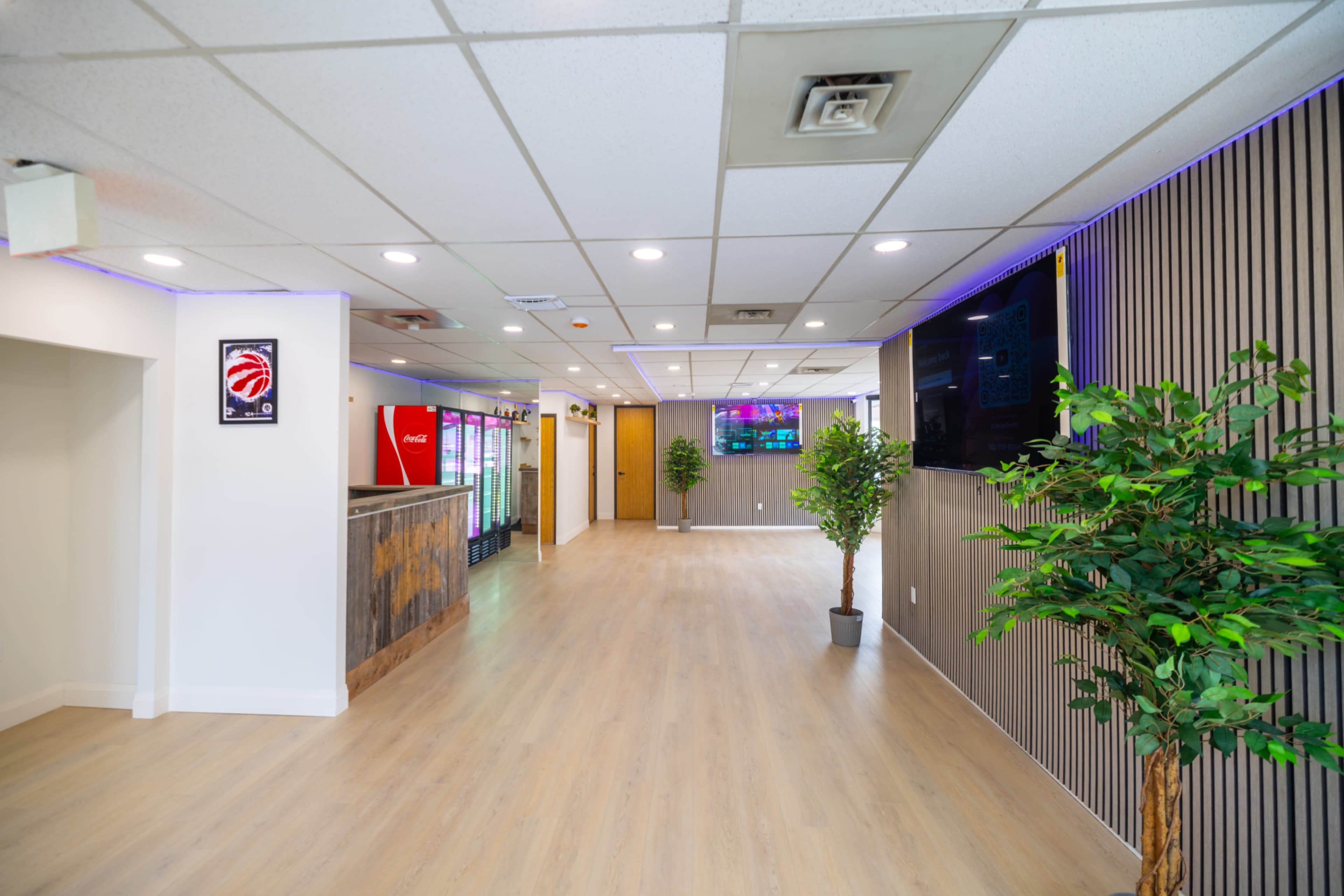 The image shows a bright and modern interior of a commercial space, featuring a reception area, soft lighting, and potted plants along the walls.