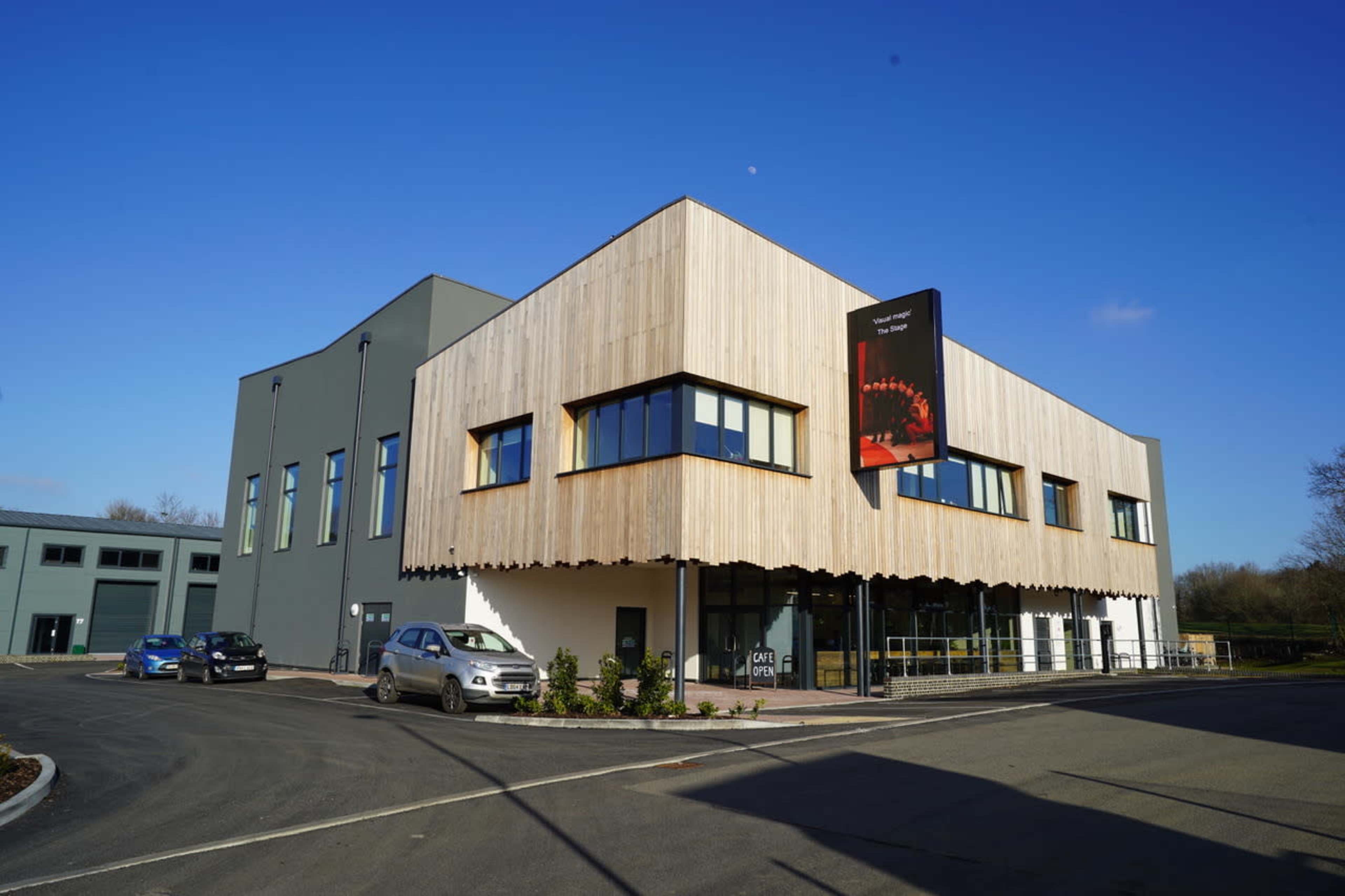 A modern building with a wooden facade and large windows, accompanied by a black banner, set against a clear blue sky.
