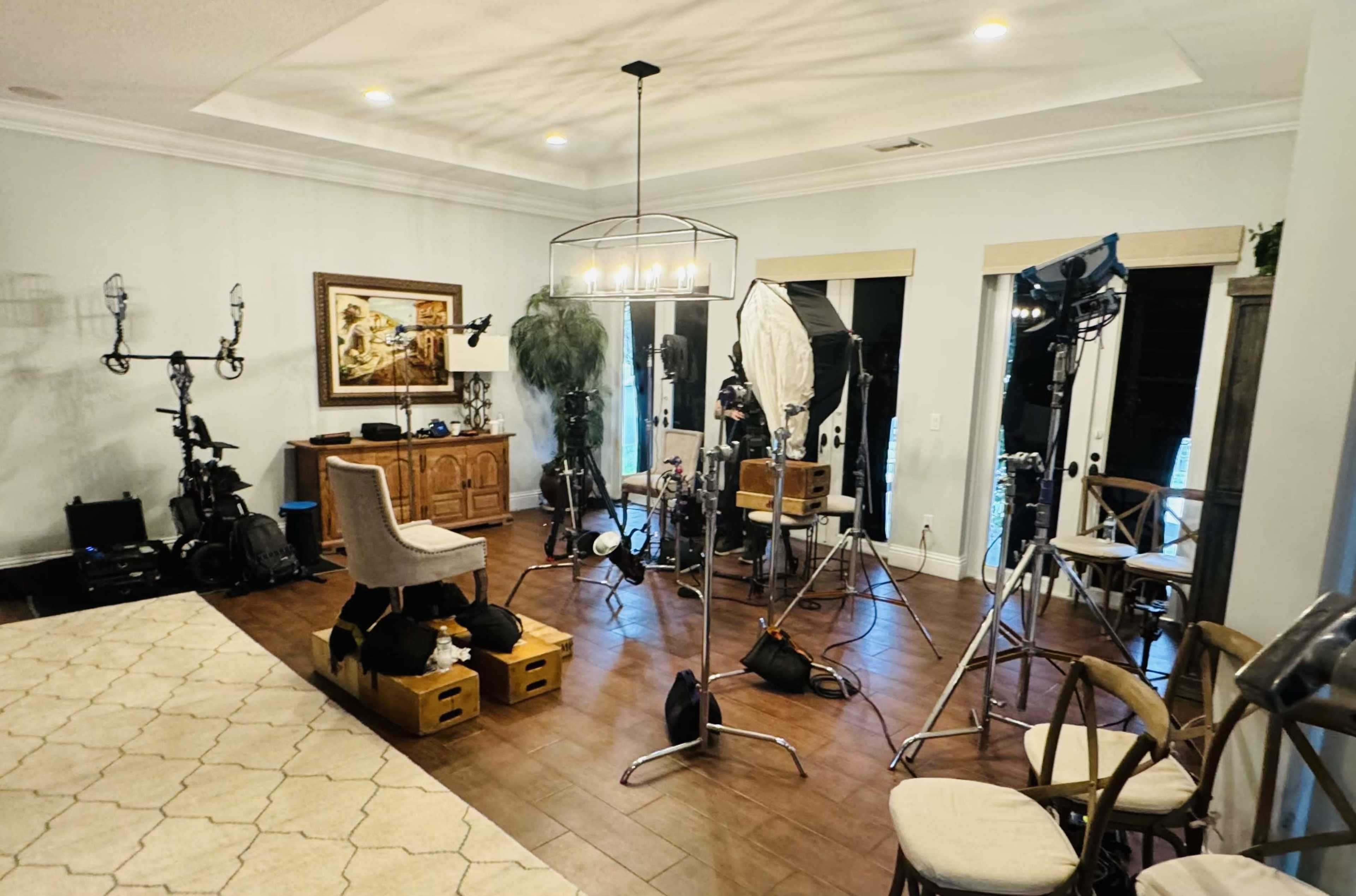A well-lit studio setup features various lighting equipment, cameras, and furniture arranged on polished wooden flooring.