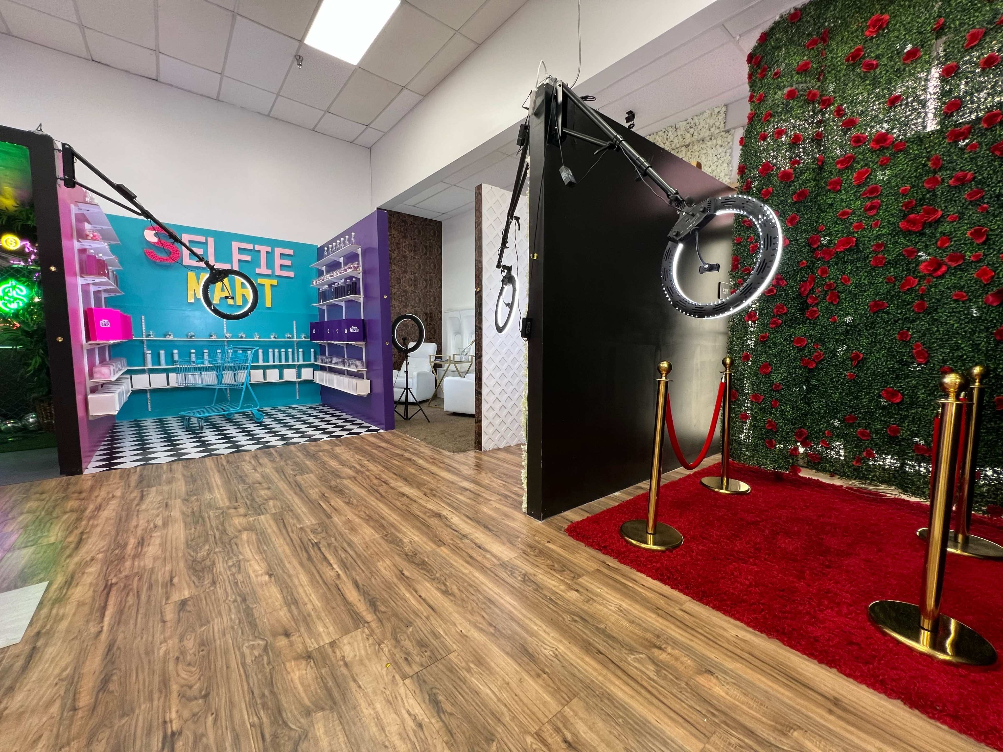 A brightly colored selfie station with a backdrop and lighting equipment, alongside a red carpet entrance and a floral wall.