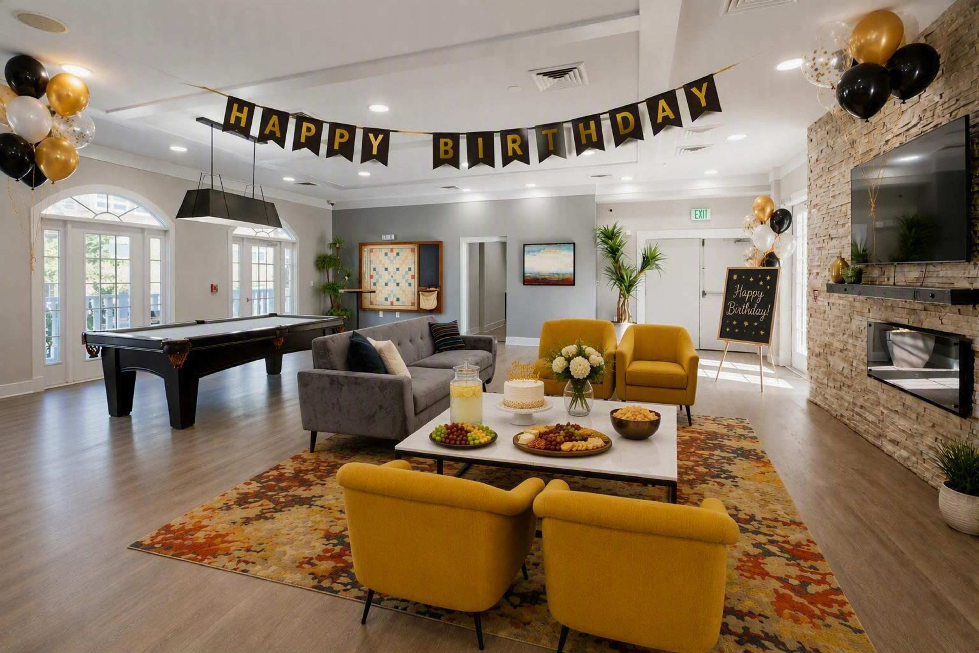 The image shows a festive interior space decorated with a "Happy Birthday" banner, featuring yellow and black balloons, a pool table, and a seating area with yellow chairs and a coffee table adorned with snacks.