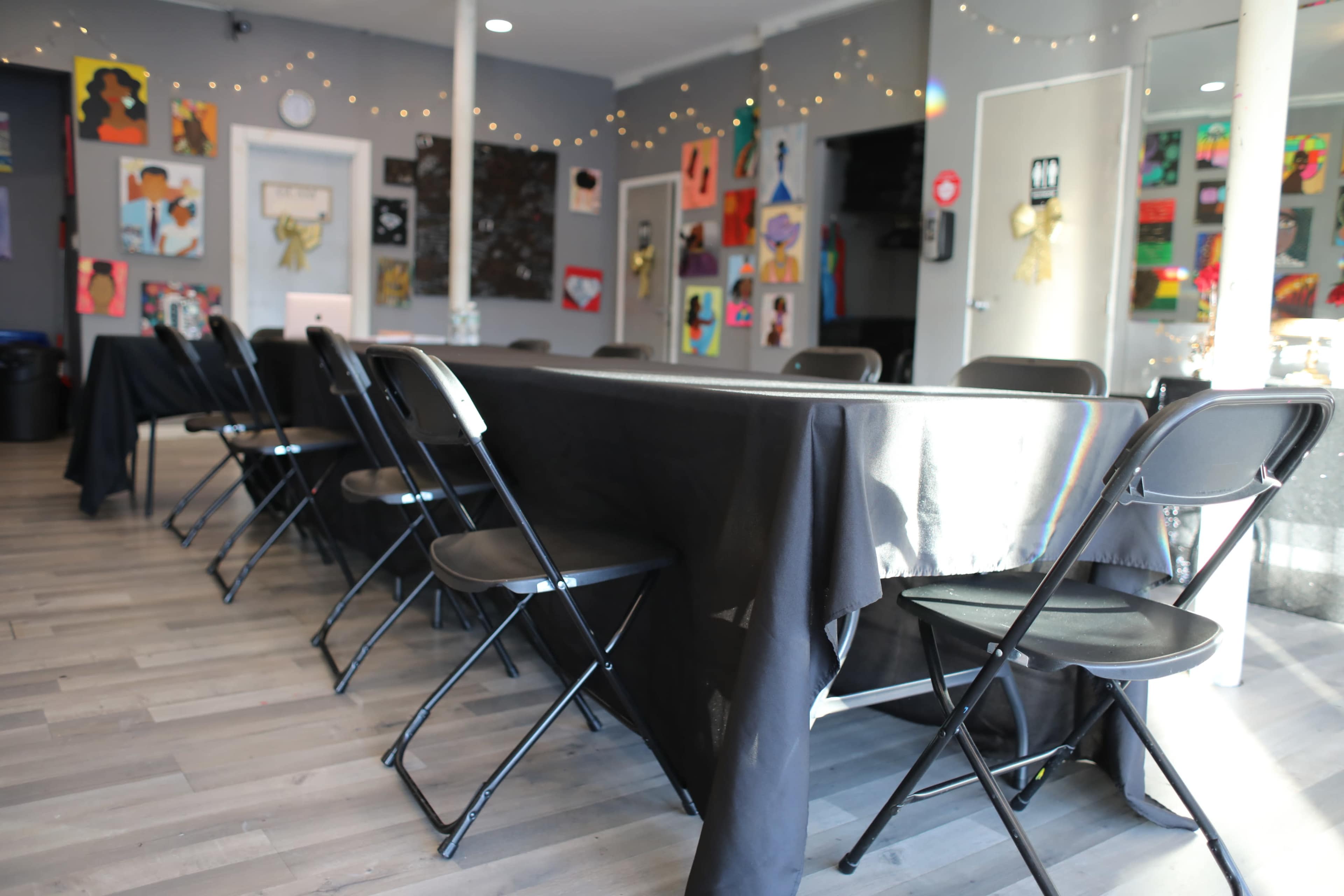 A spacious room with several black tables and chairs set up, adorned with colorful art displayed on the walls.
