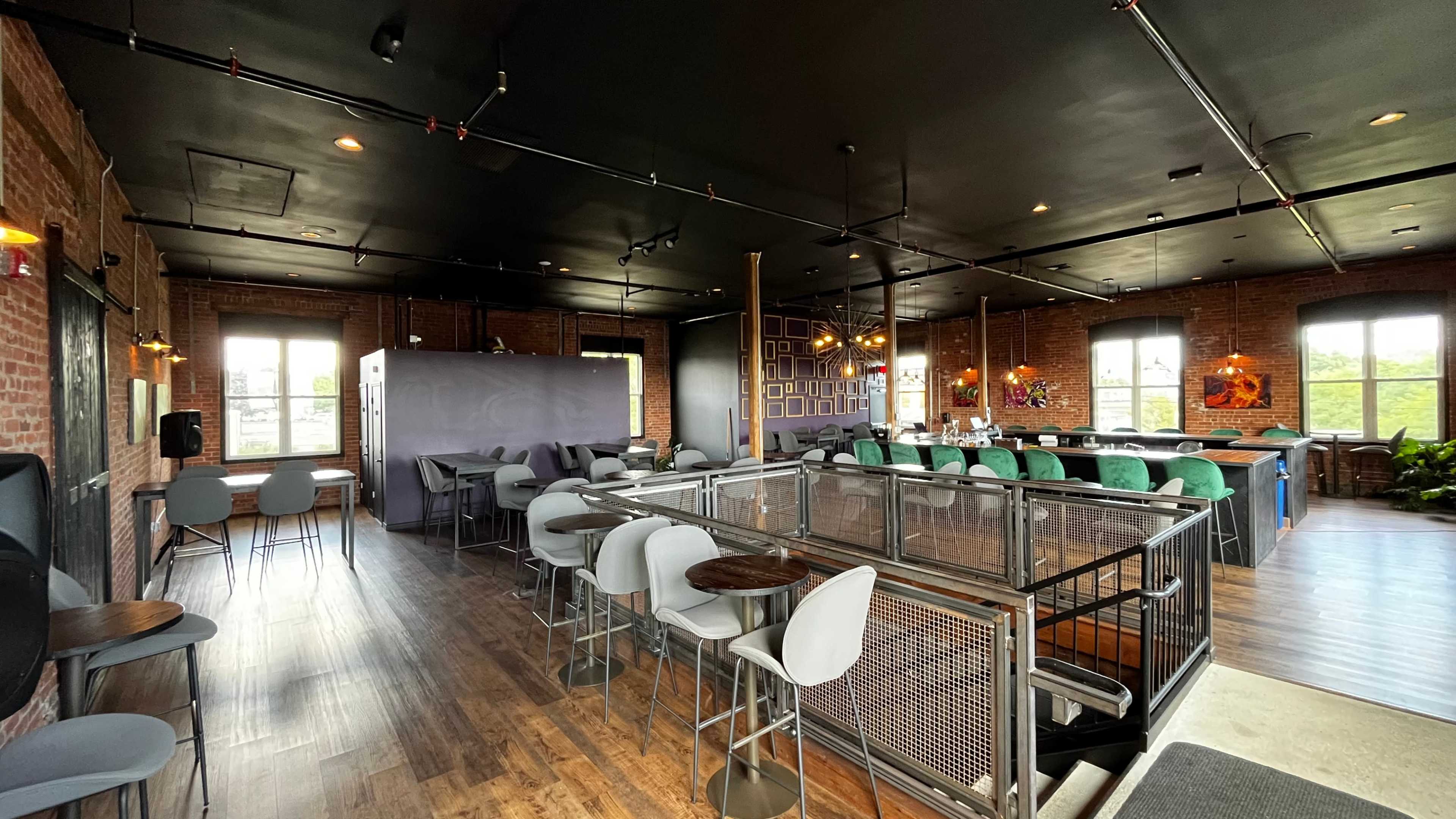 A spacious, modern interior of a restaurant or bar with brick walls, various seating options, and large windows providing natural light.