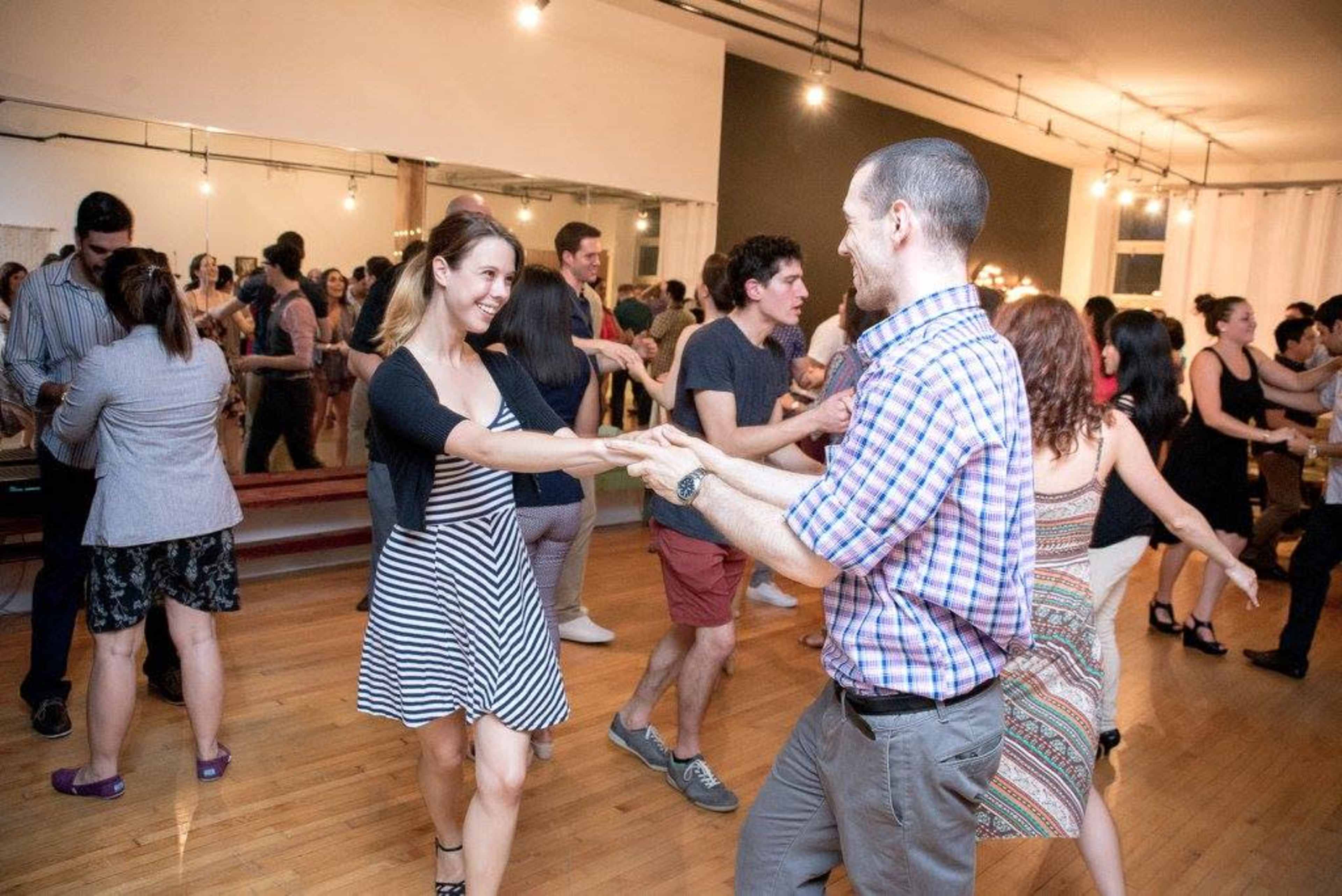 A lively dance event is taking place in a spacious studio filled with people dancing in pairs.