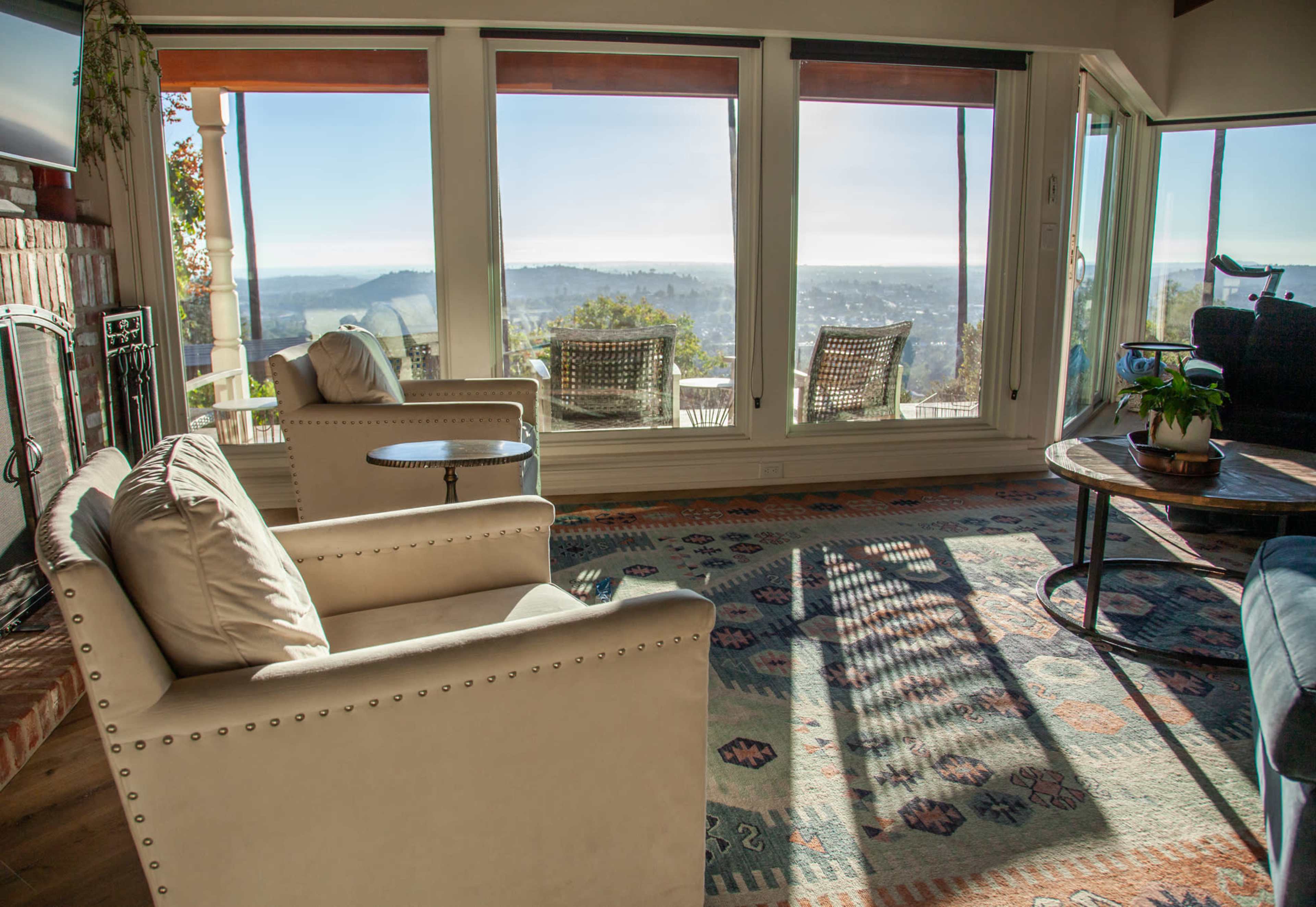 A cozy living room features two armchairs, a small table, and large windows showcasing a panoramic view of the landscape outside.