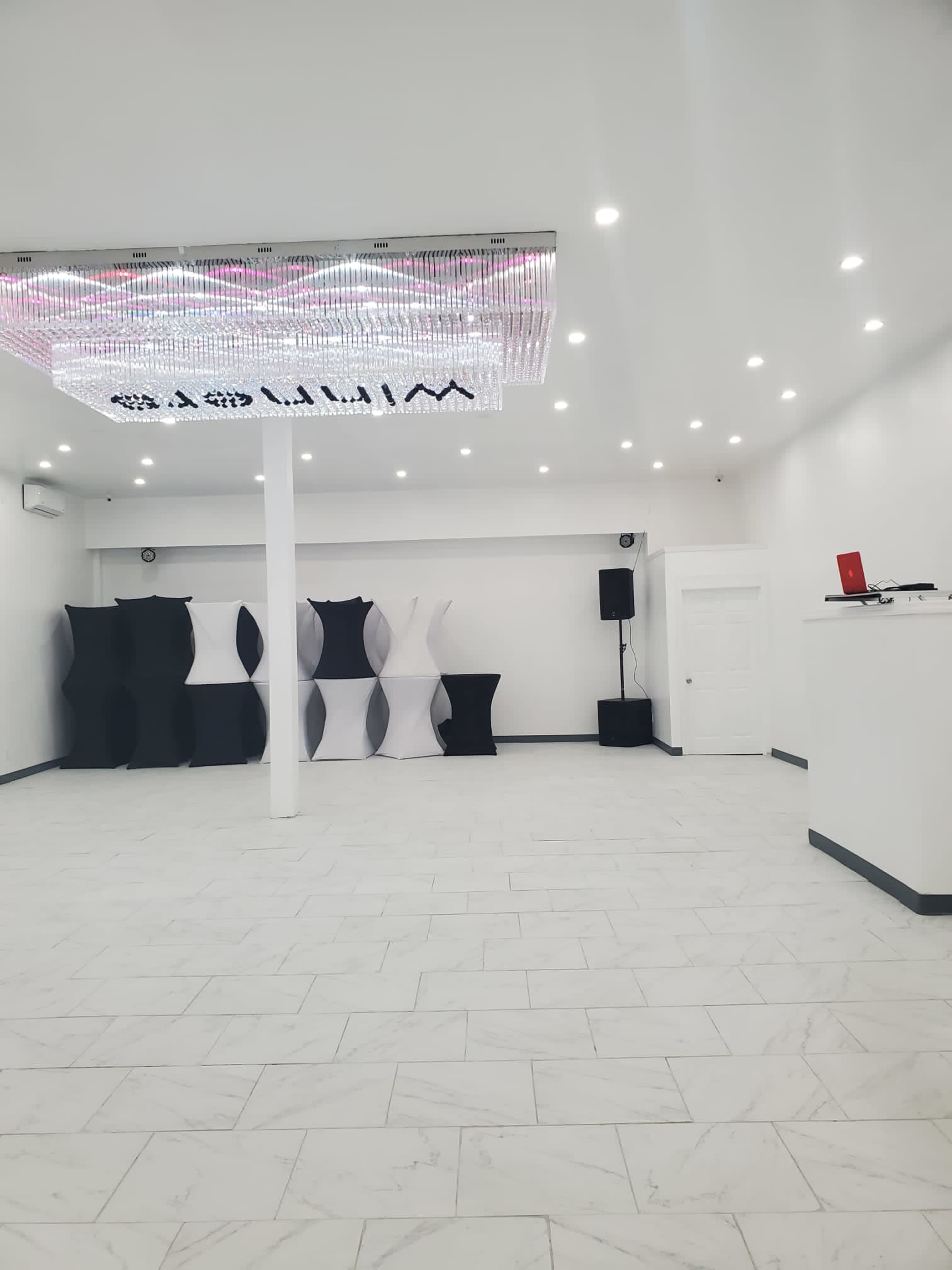 The interior of a spacious, modern room features a chandelier, white walls, and black and white display structures.