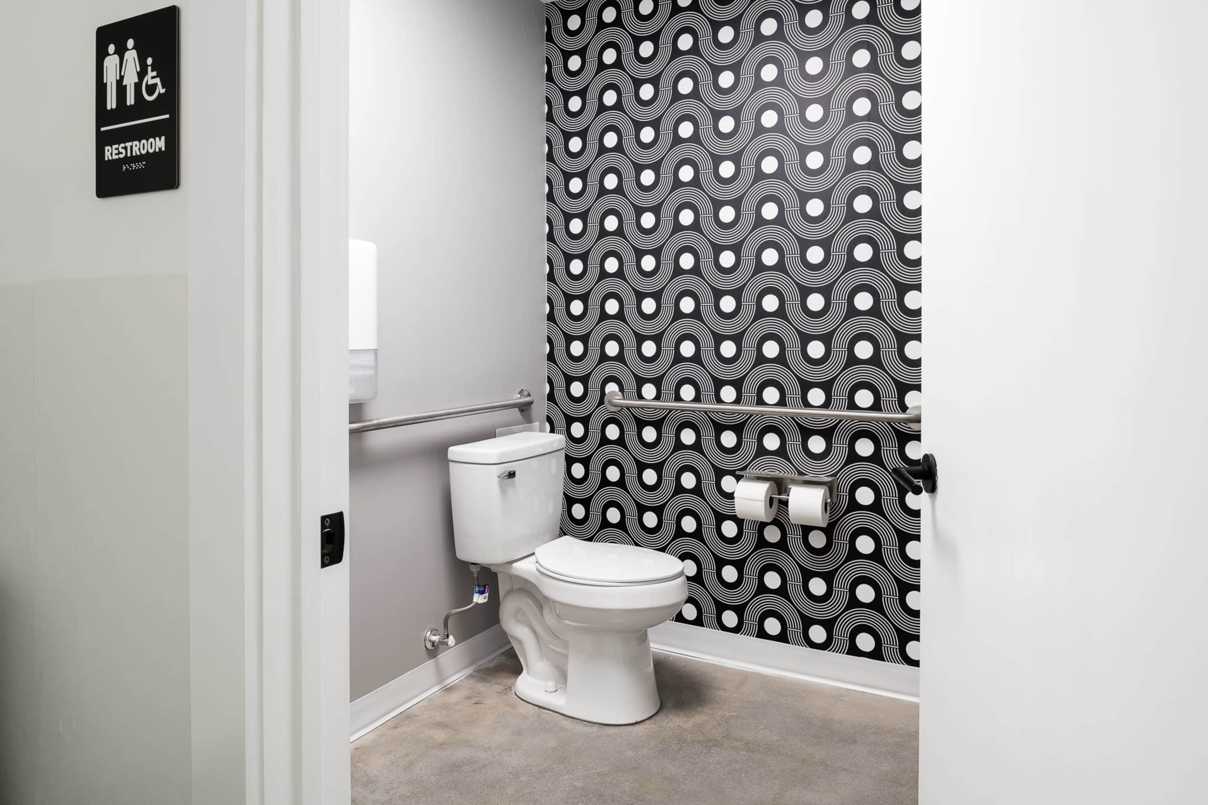 The image shows a restroom with a modern black and white patterned wall, featuring a toilet, toilet paper holder, and a hand dryer.