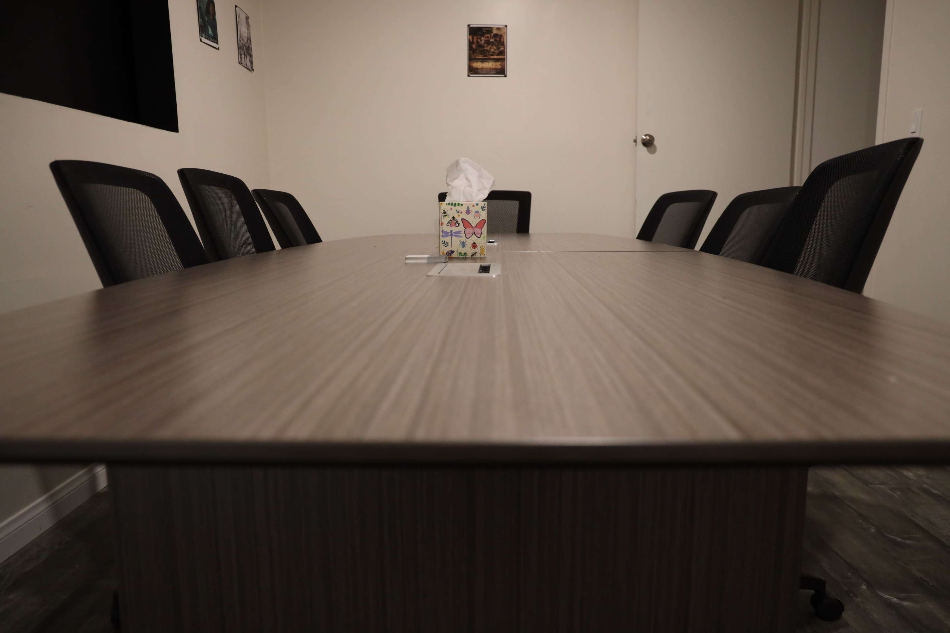 A conference room with a large wooden table surrounded by several black chairs and a box of tissues in the center.