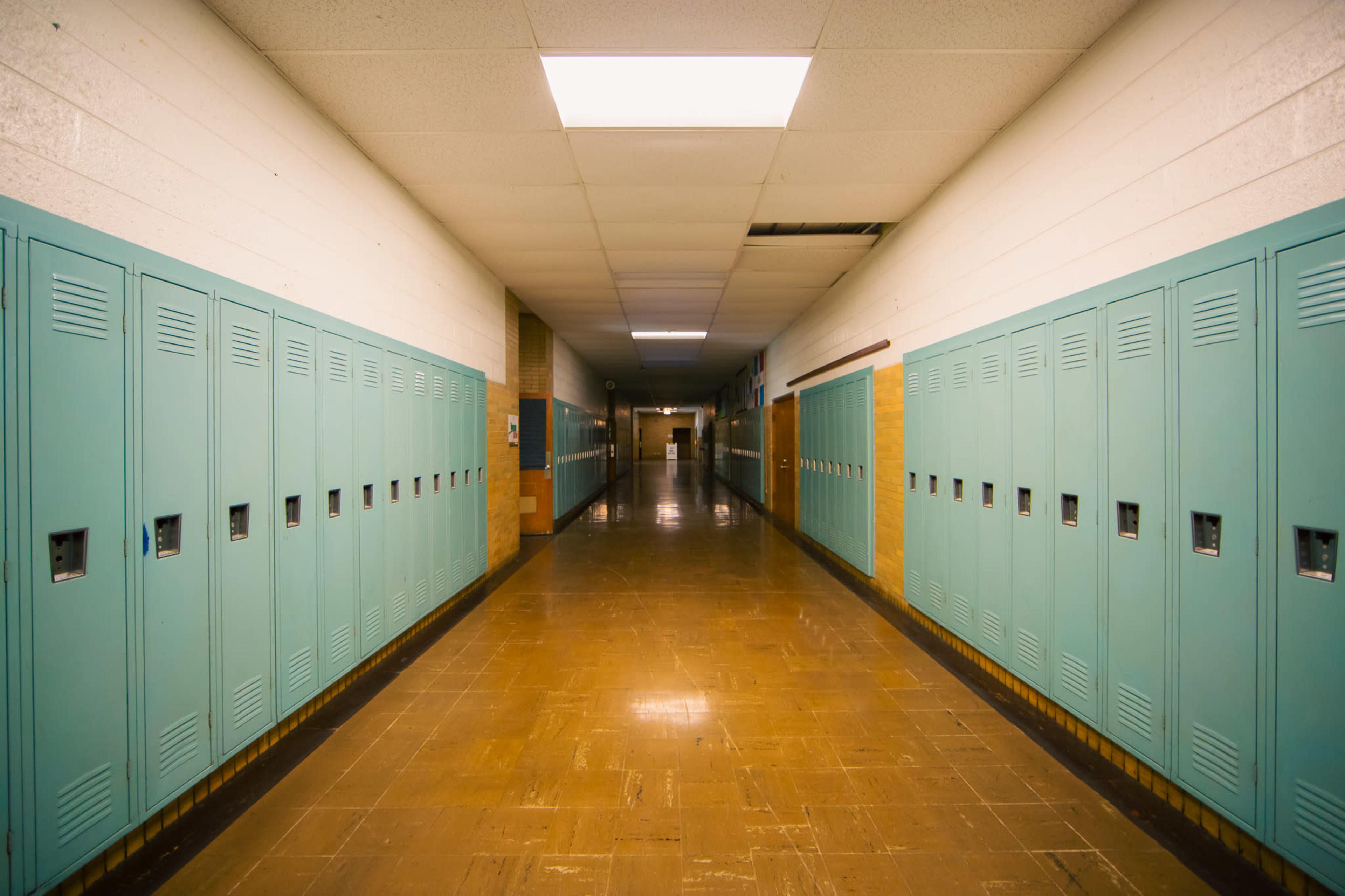 The image shows a narrow school hallway lined with turquoise lockers on both sides.