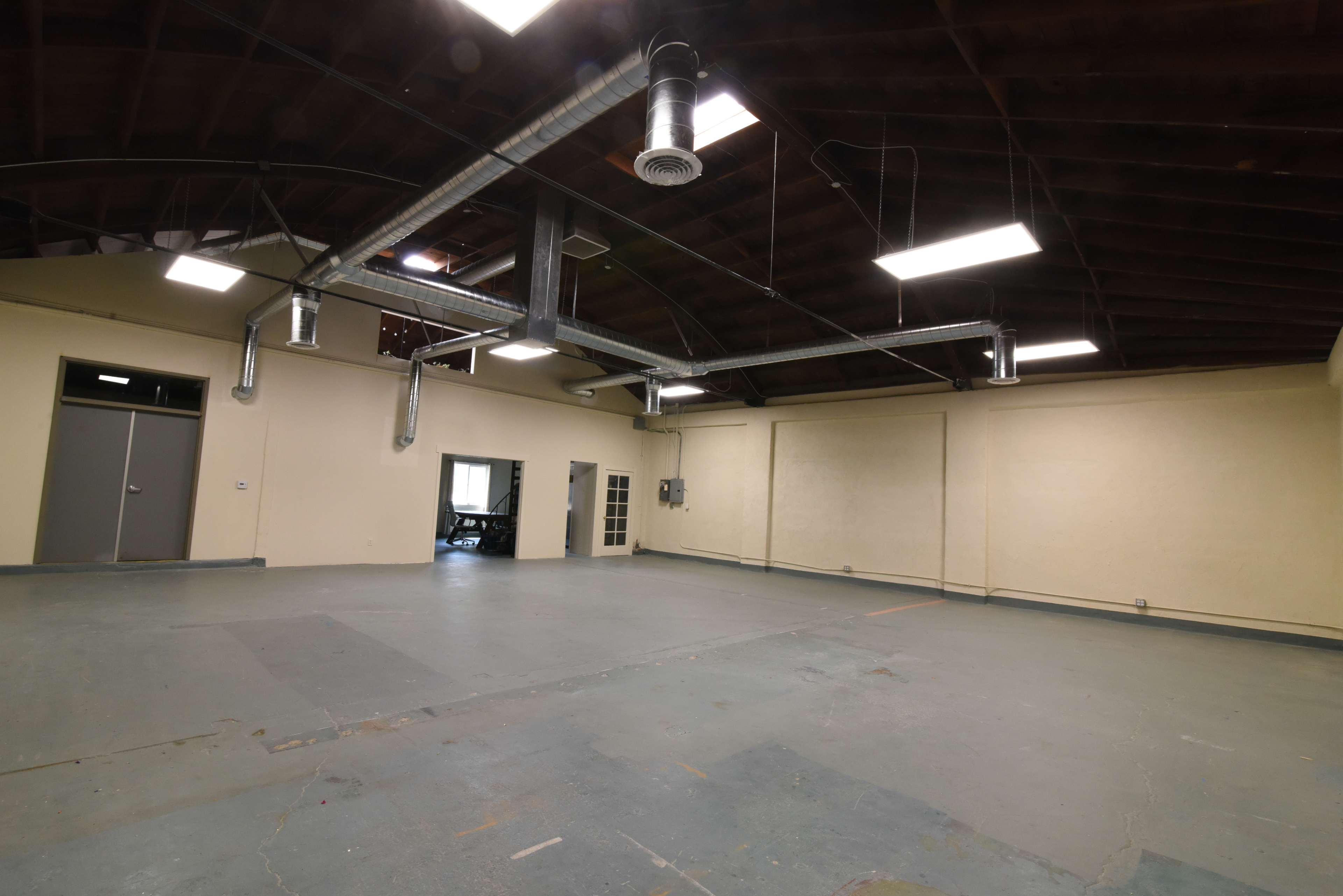 A large, empty room with exposed beams, ductwork, and a doorway leading to another space.