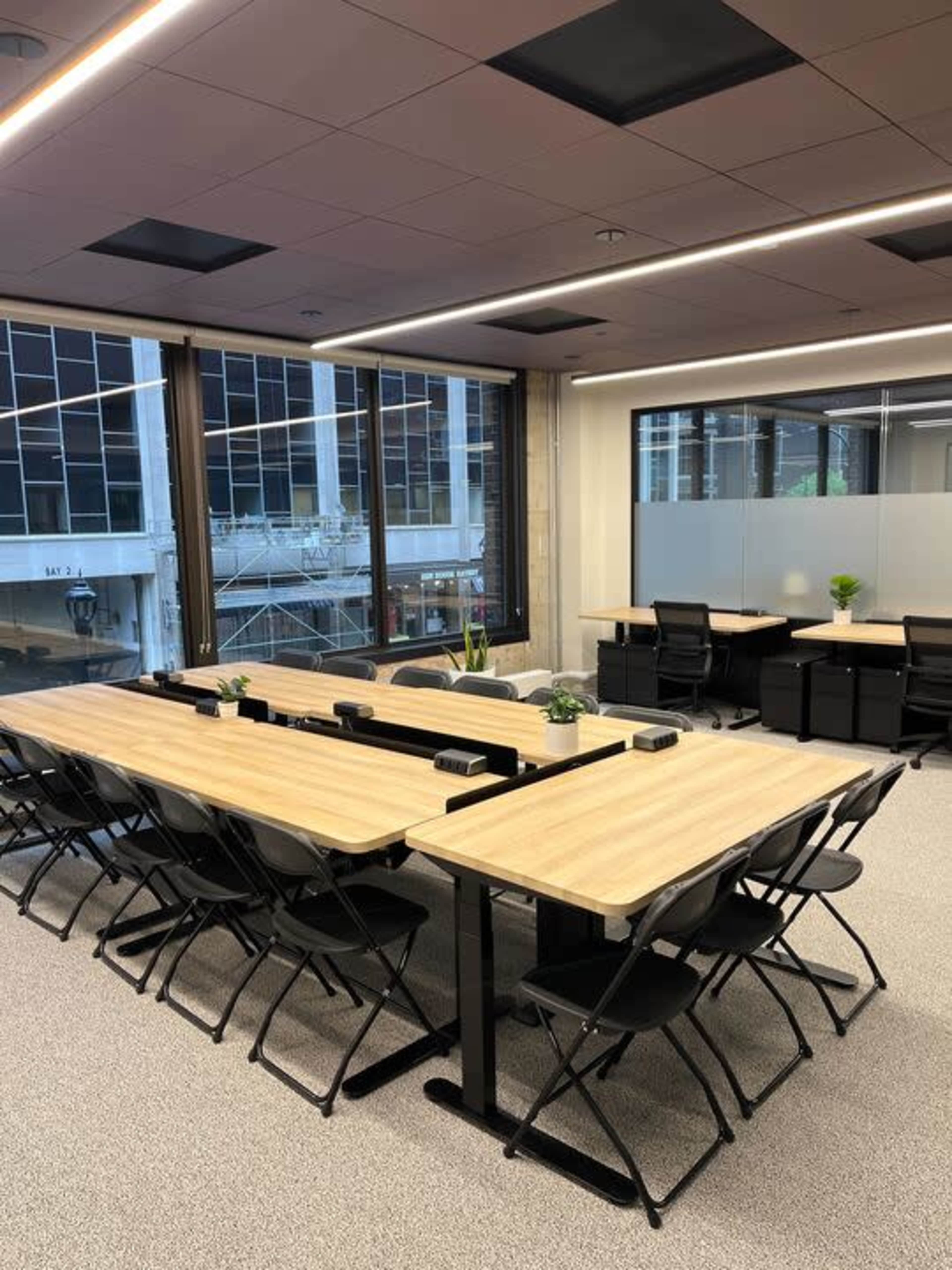 A modern office space with several tables arranged in a meeting format, surrounded by large windows.