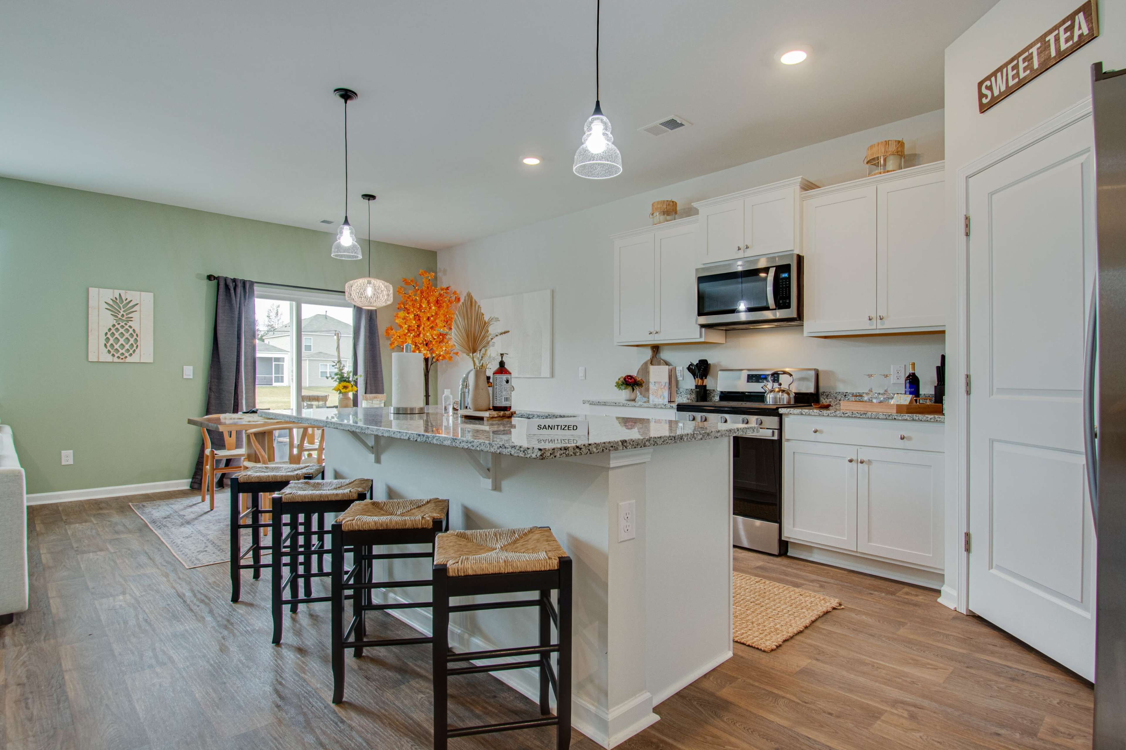 A modern kitchen with white cabinets, stainless steel appliances, a granite island, and bar stools, featuring a cozy dining area with natural light.