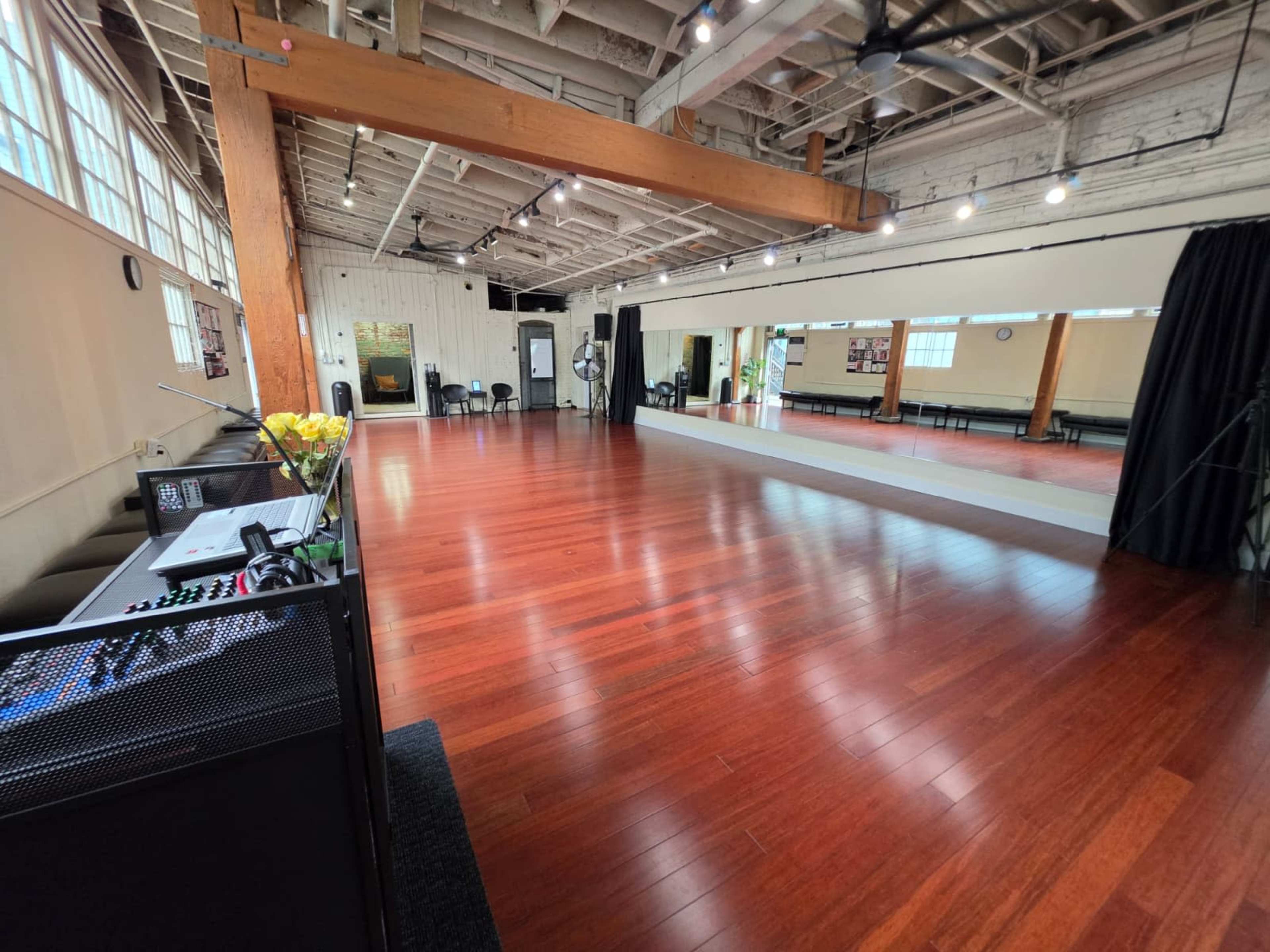 The image shows a spacious dance studio with hardwood floors, large windows, and a mirrored wall.