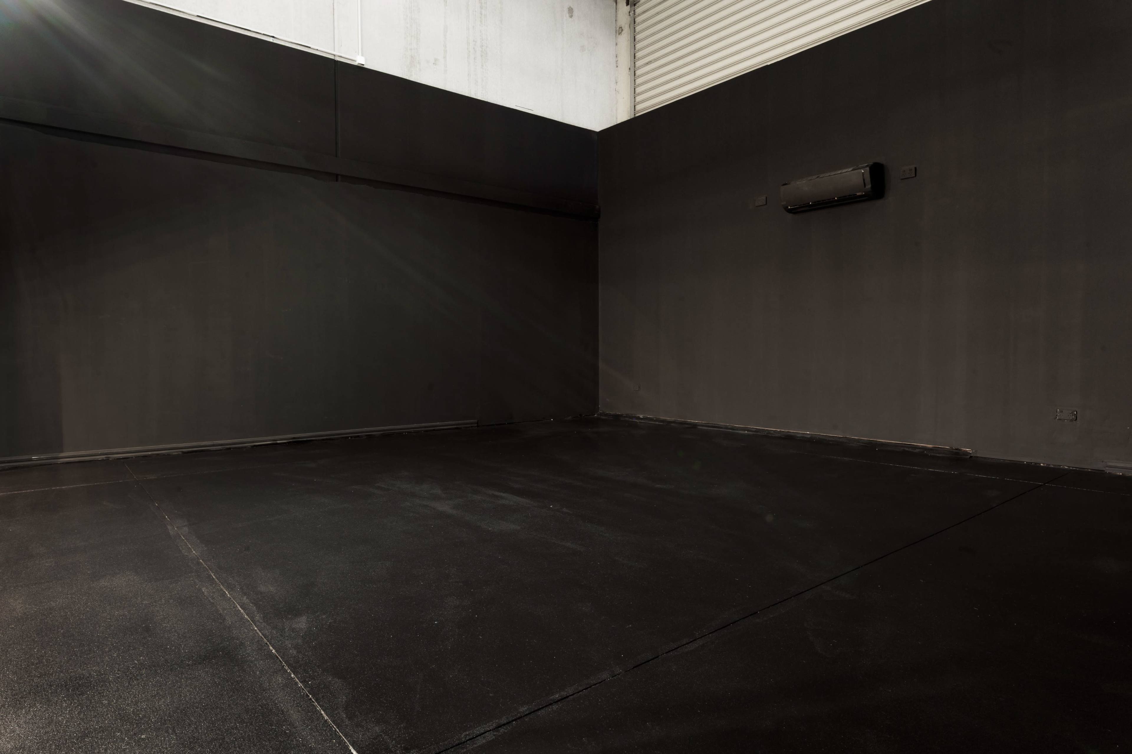 The image shows an empty, dark room with black walls and a floor, featuring a single air conditioning unit mounted on one wall.