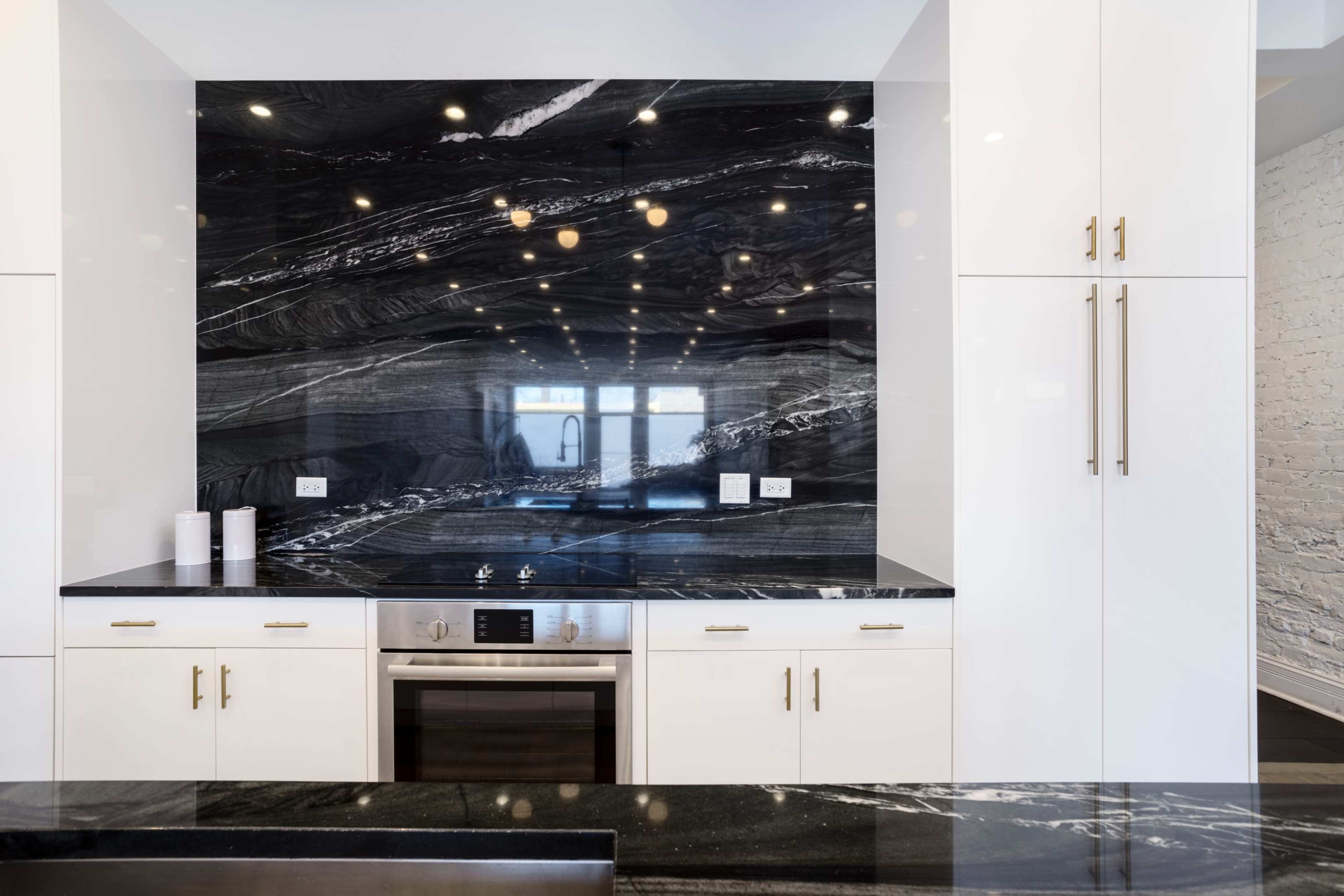 A modern kitchen with white cabinets, a black and white marble backsplash, and stainless steel appliances.
