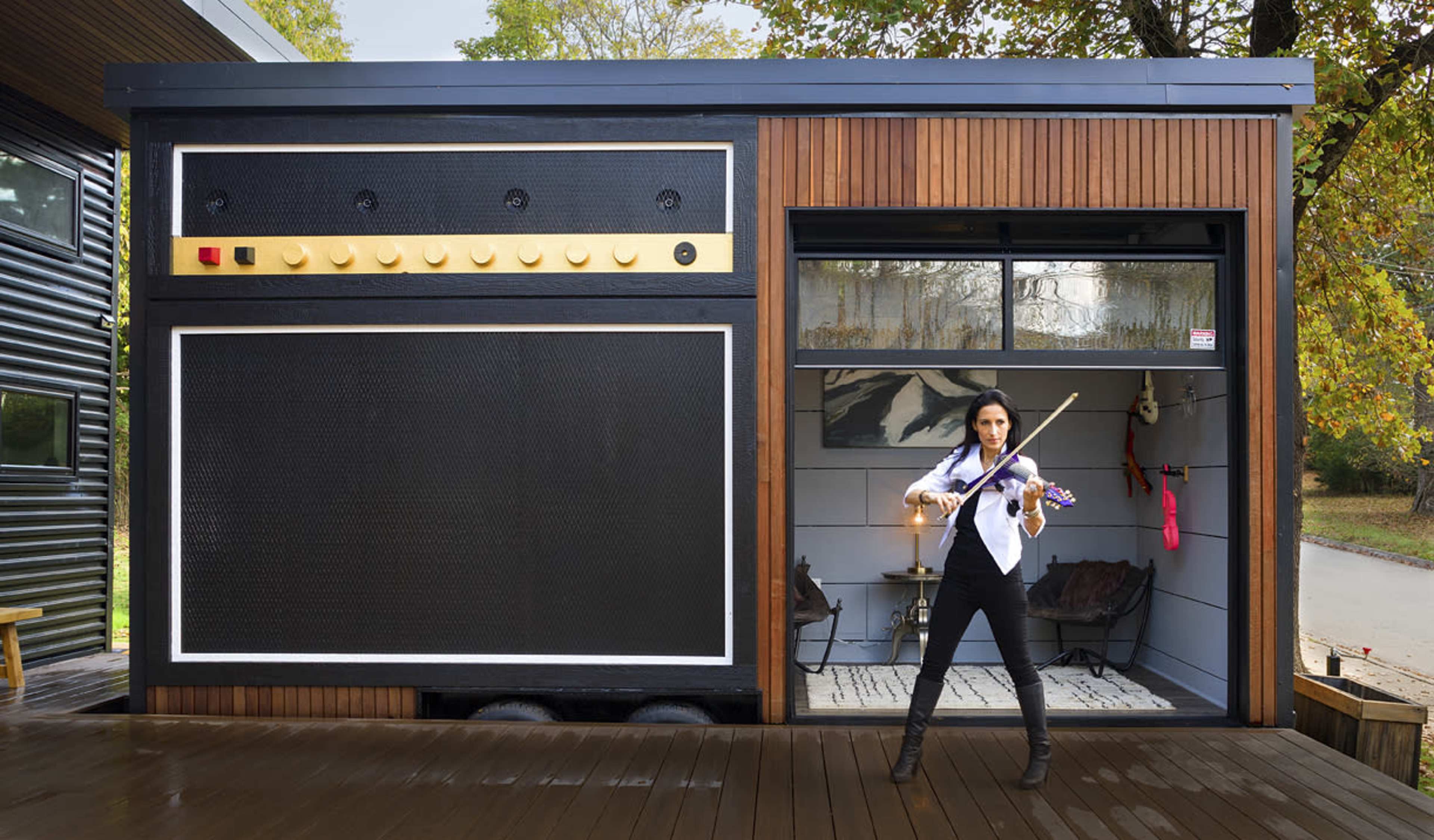 A woman plays a violin in front of a building designed to resemble a large guitar amplifier.