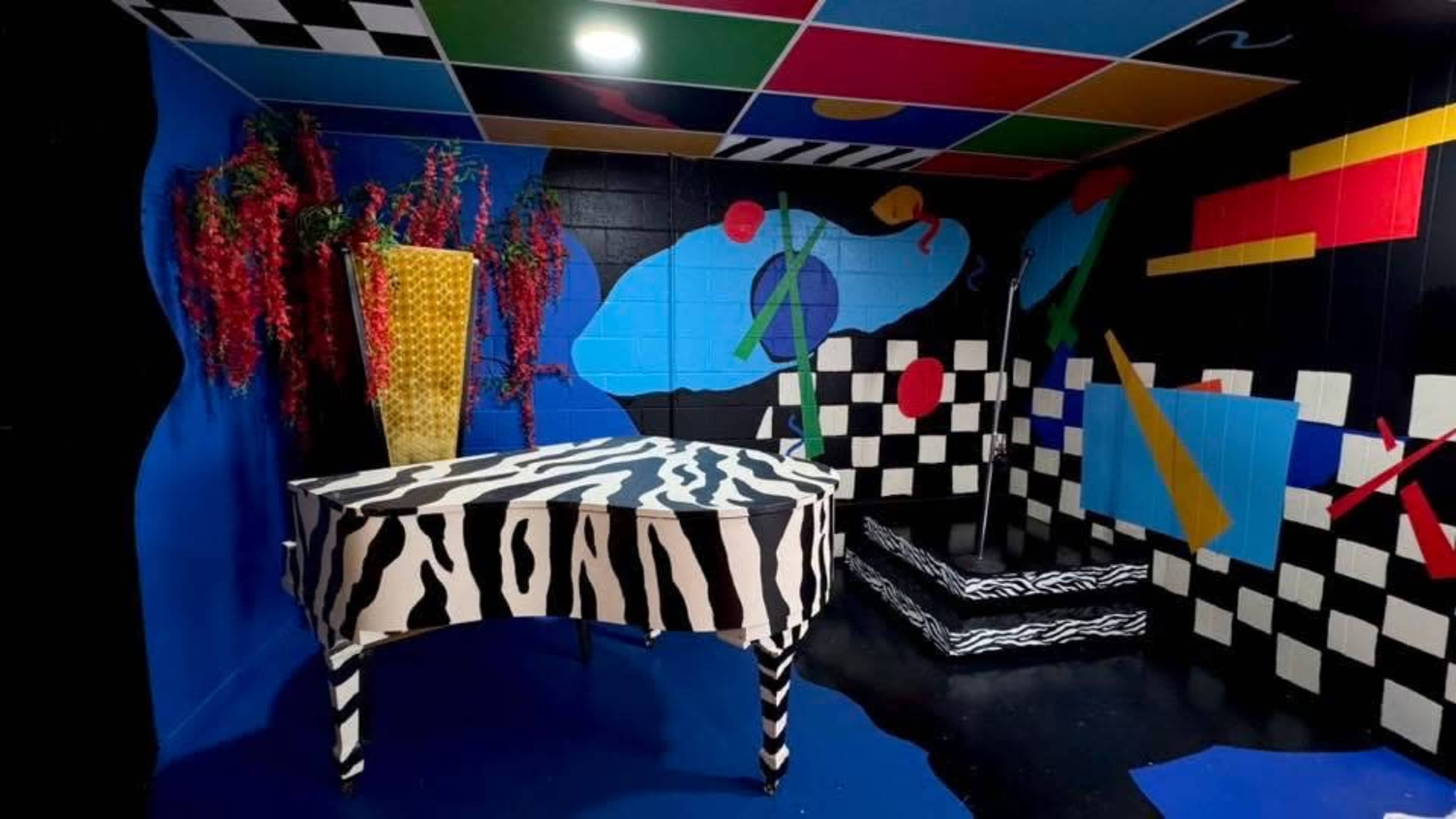 The room features a zebra-striped piano surrounded by brightly colored geometric patterns on the walls.