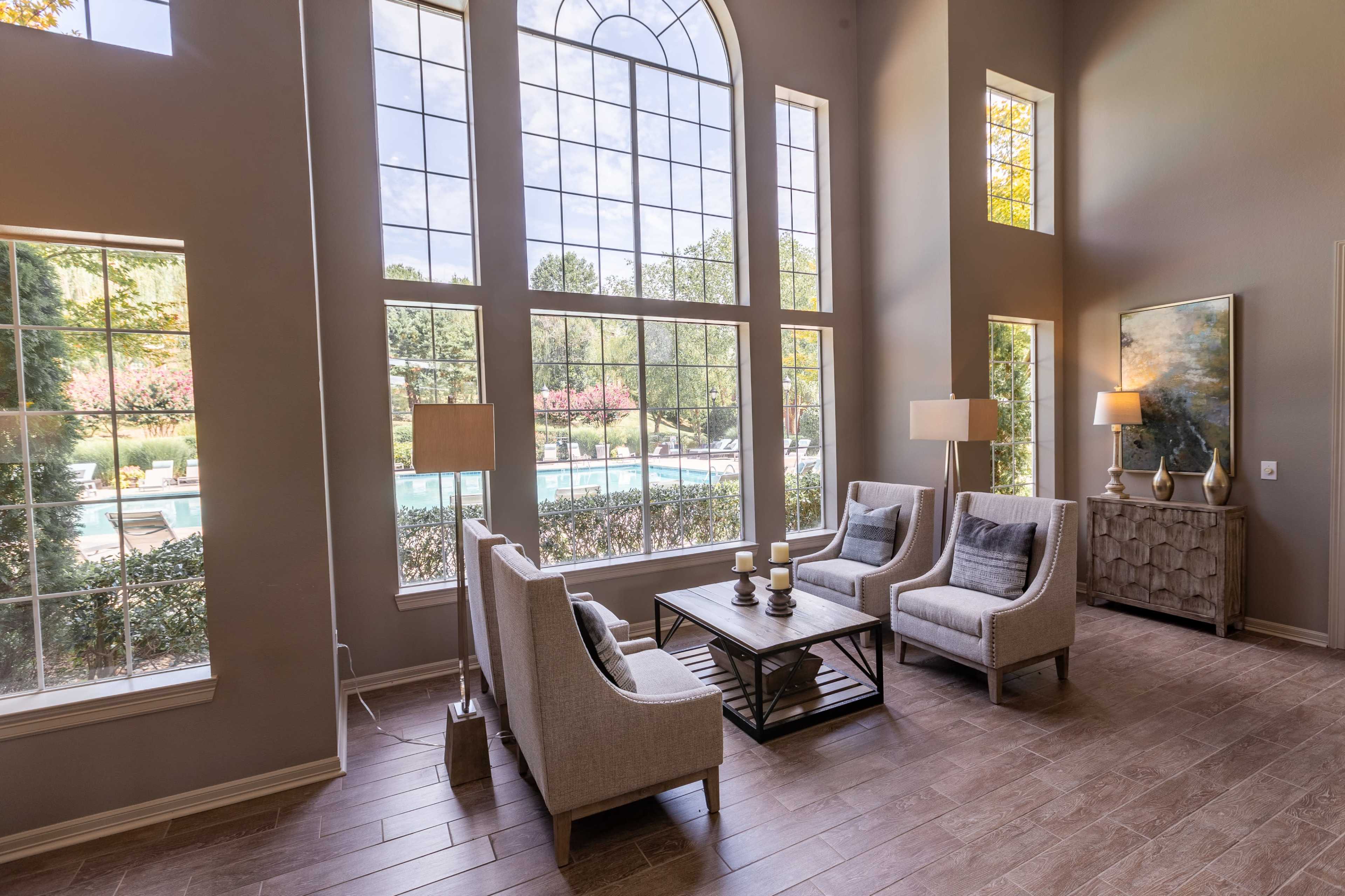 The image shows a modern living area with large windows overlooking a pool and landscaped yard, featuring two armchairs and a coffee table.