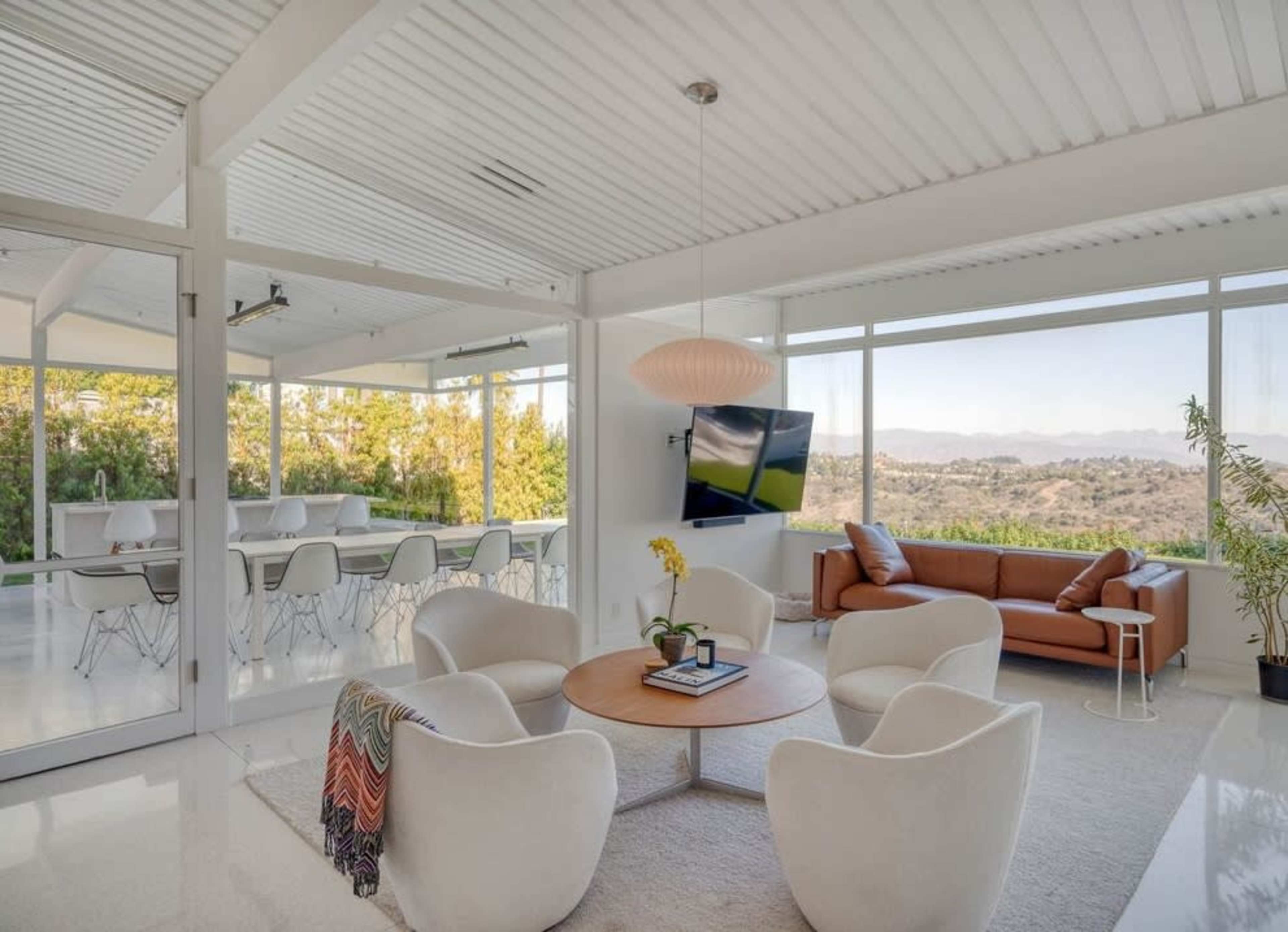 A modern living space features a circular seating arrangement around a coffee table, with large windows showcasing a scenic outdoor view.