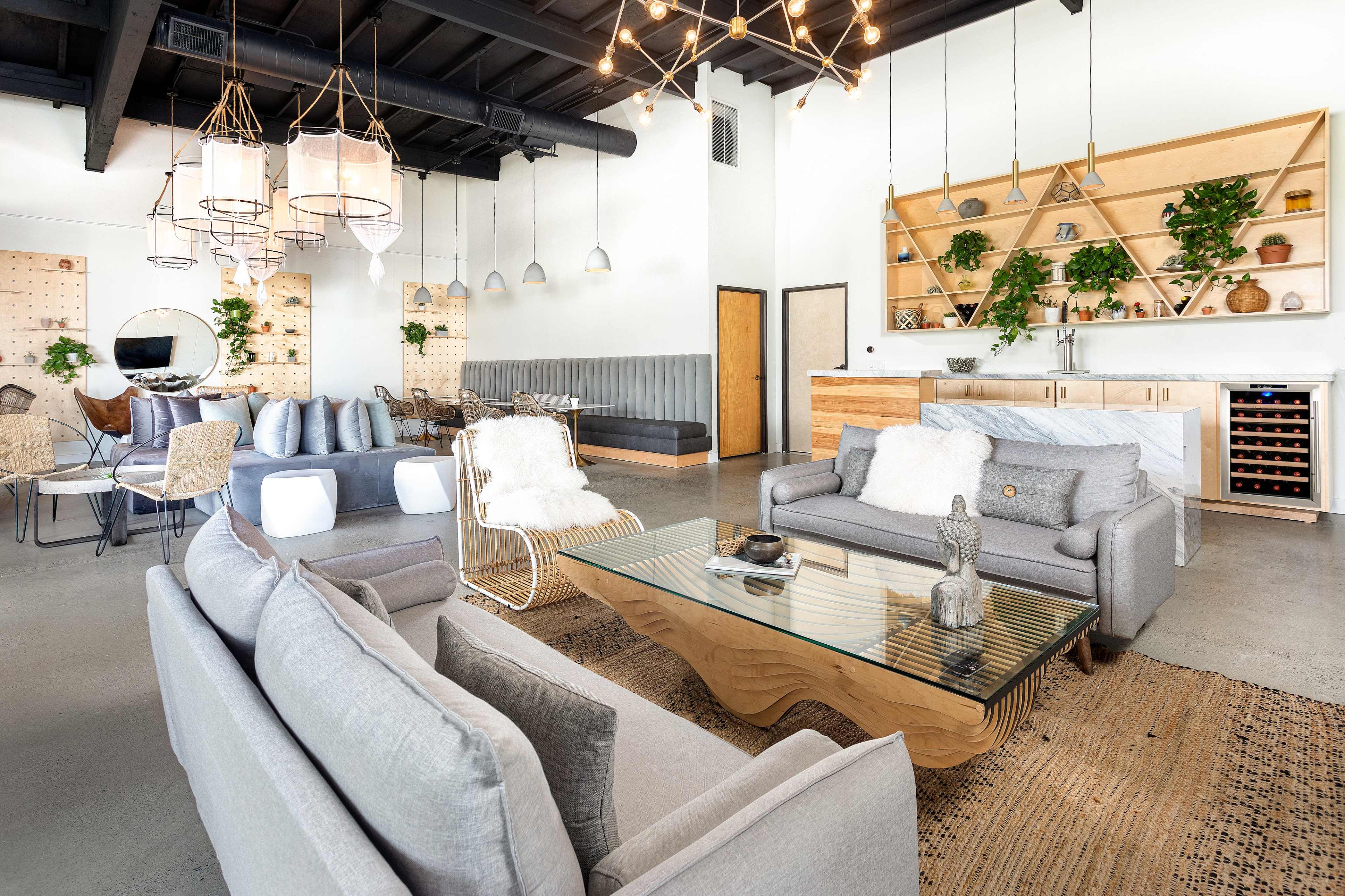 A modern lounge area featuring gray sofas, a wooden coffee table, decorative plants, and a dining set in a well-lit space with geometric lighting fixtures.