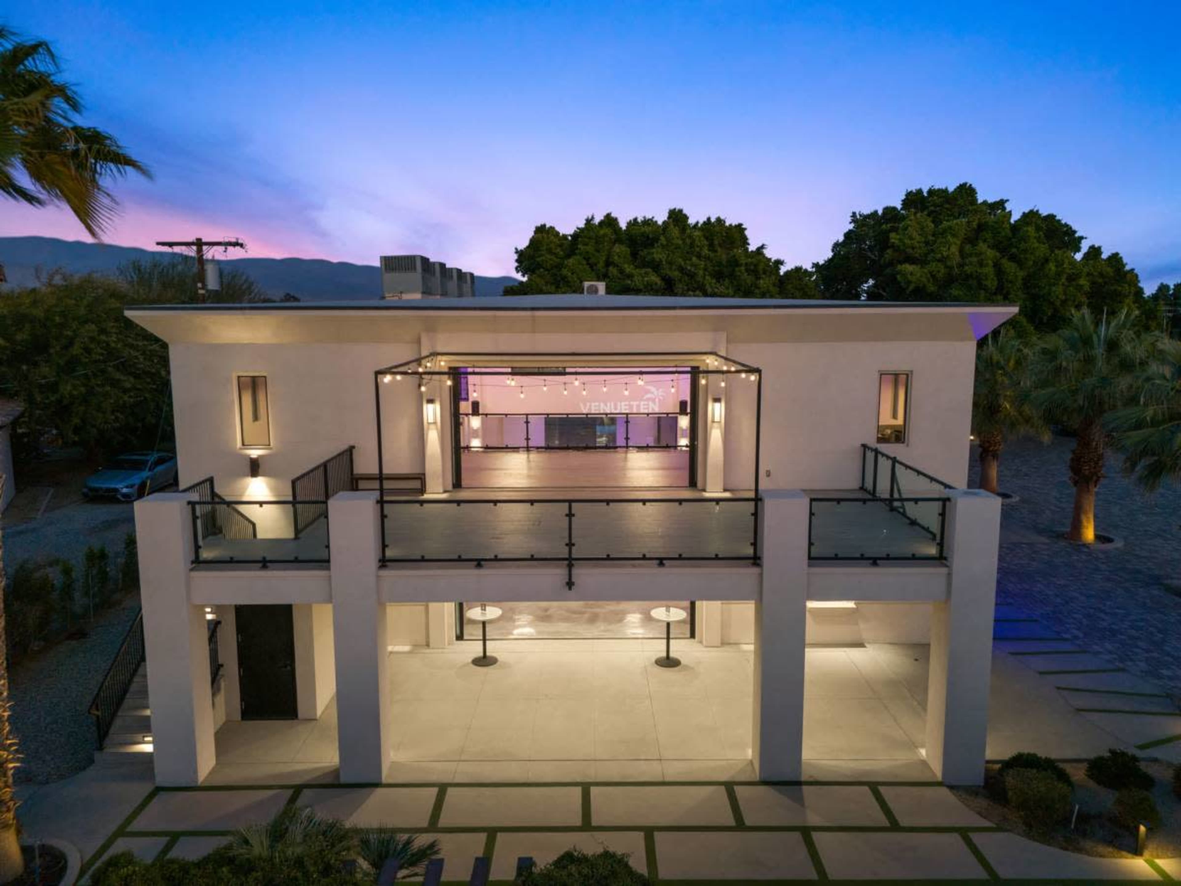 A modern, two-story building features a spacious balcony with an open area and palm trees surrounding the property.