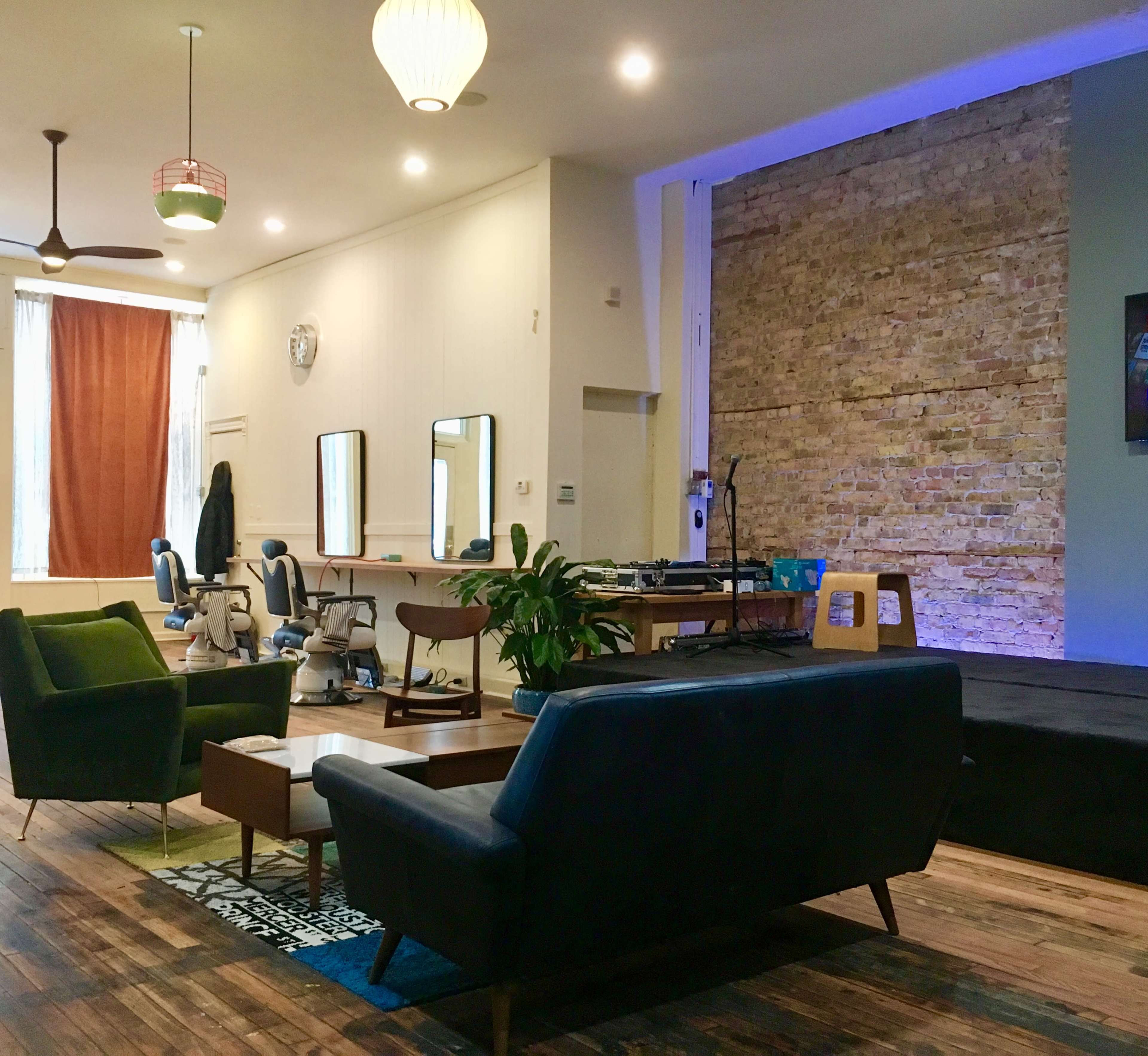 The image shows a contemporary salon interior with seating areas, a stage, and brick walls.