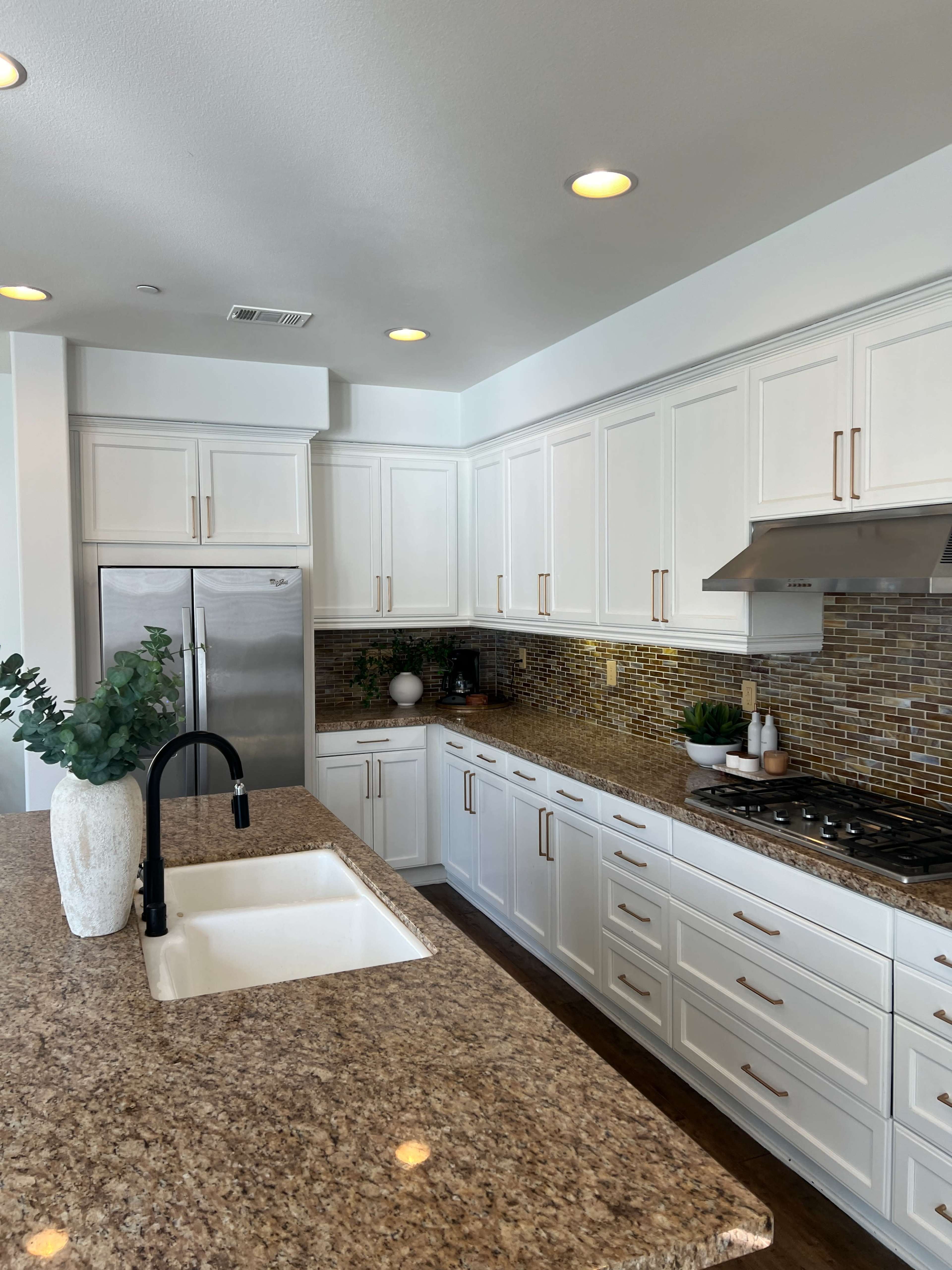 The kitchen features white cabinetry, a granite countertop, stainless steel appliances, and a mosaic tile backsplash.