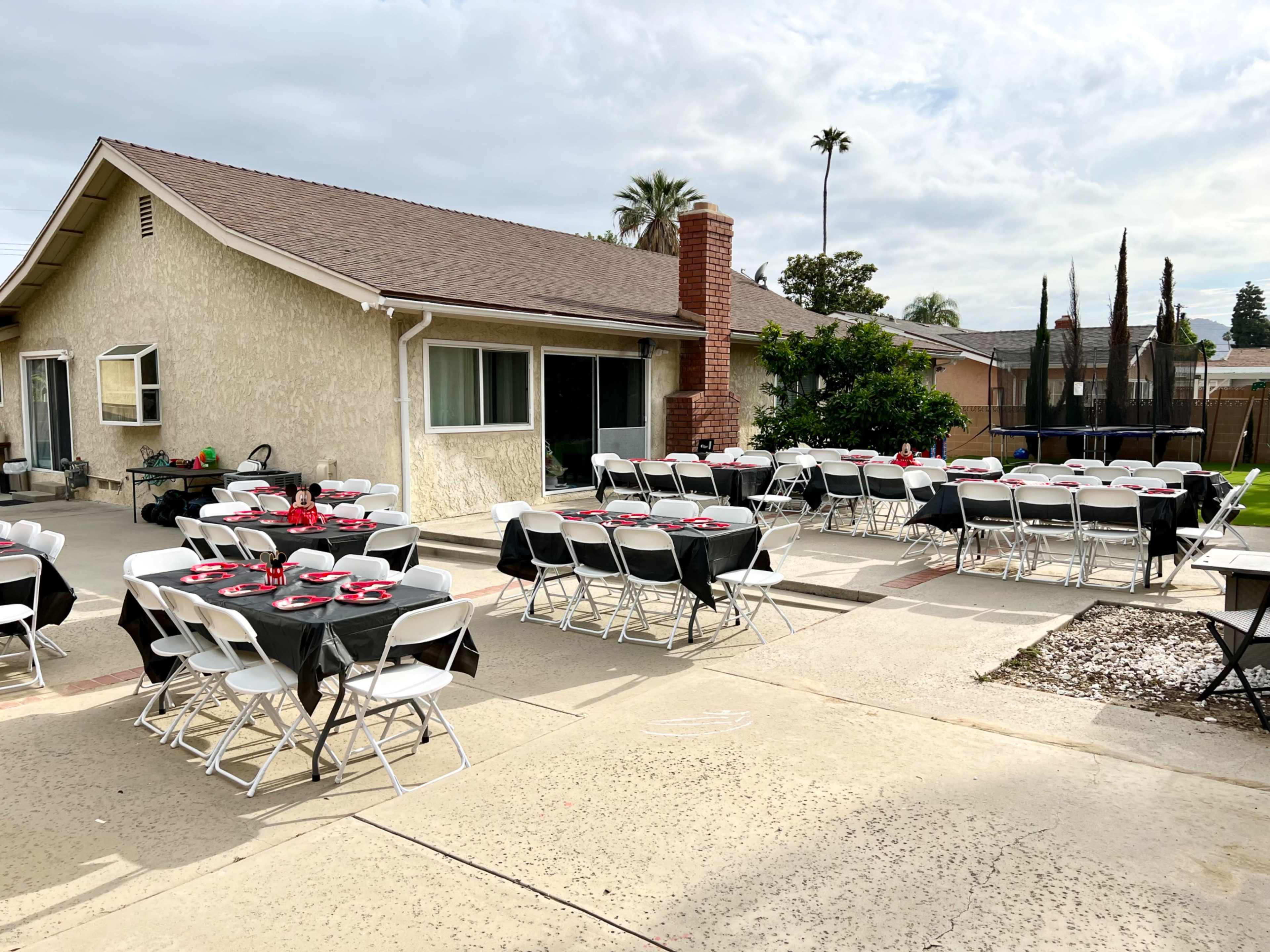 A patio is set up for an outdoor event with several tables covered in black tablecloths and red decorations.