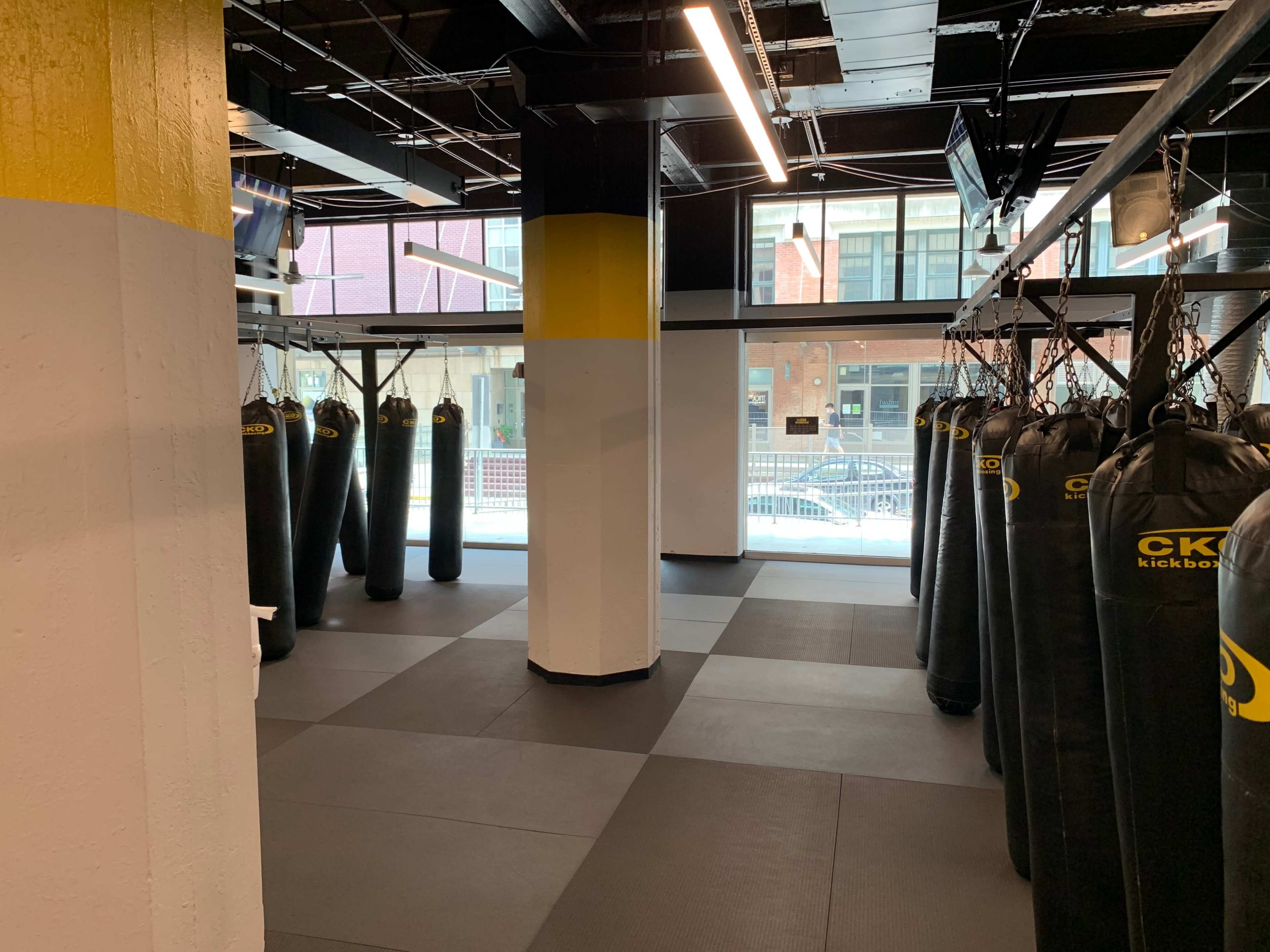 A spacious kickboxing studio featuring multiple hanging punching bags, with large windows letting in natural light.