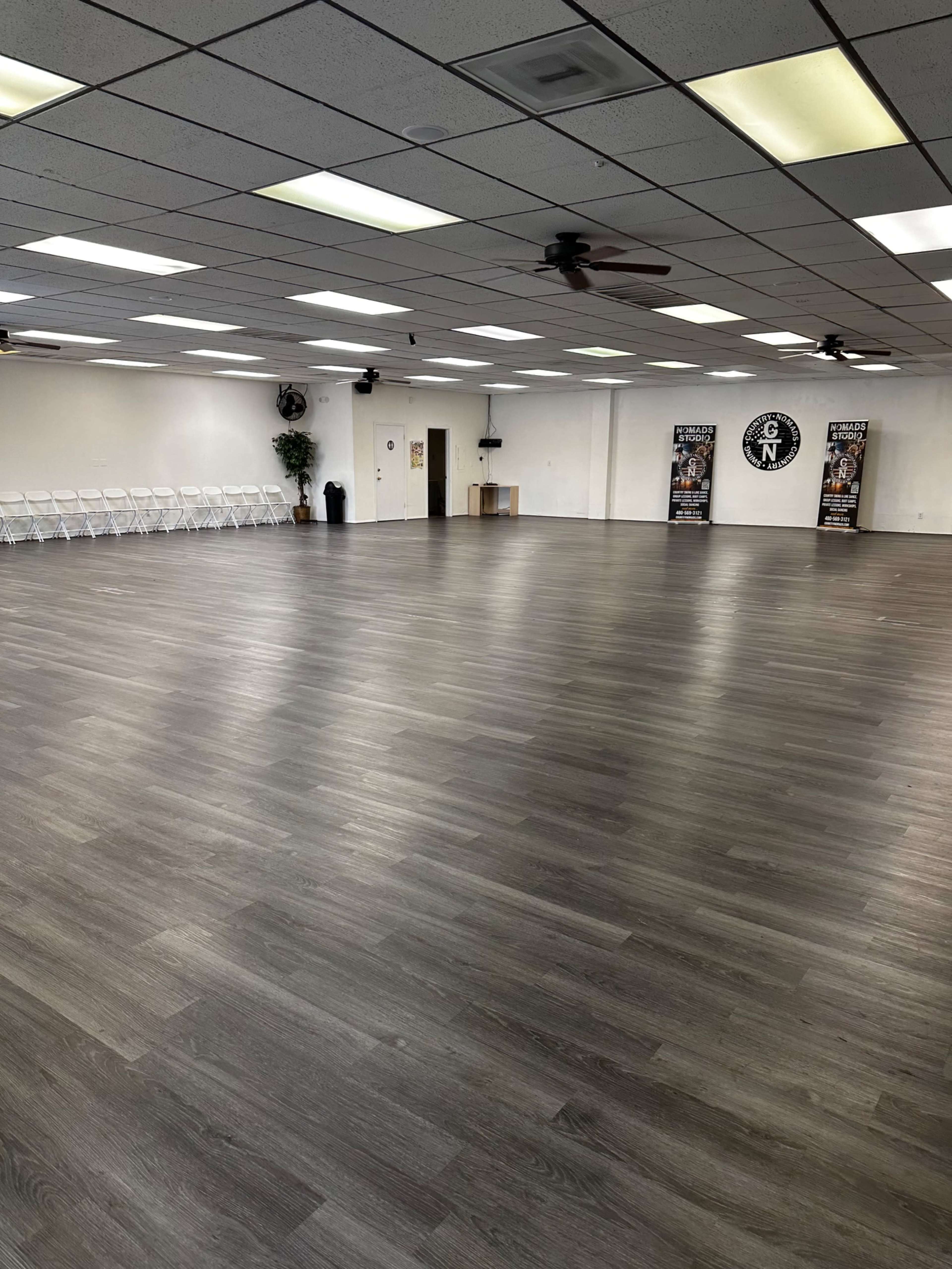 A large indoor space with a polished wooden floor, empty folding chairs along one wall, and two banners in the background.