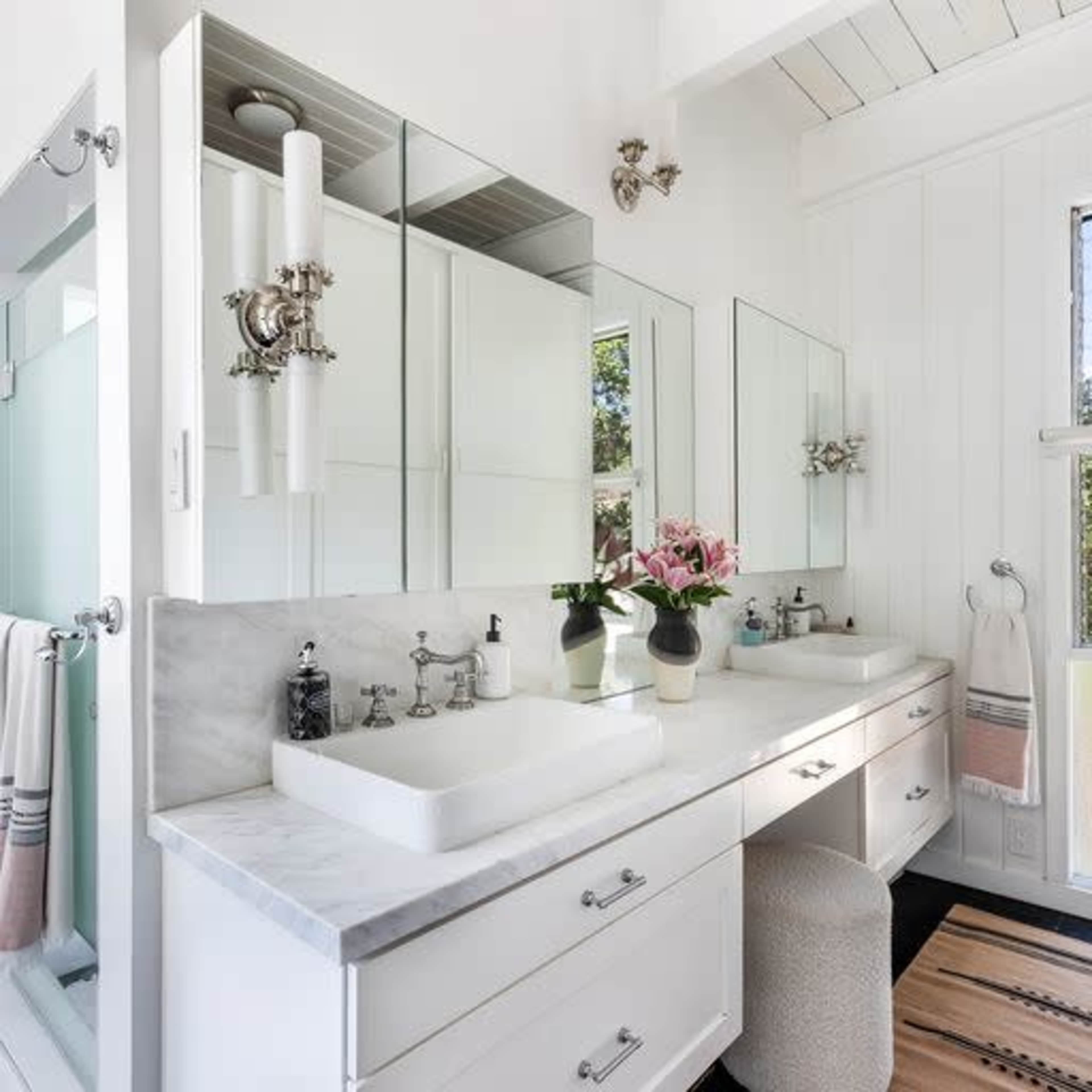A modern bathroom with a marble countertop, dual sinks, and a large mirror, featuring light fixtures and plants for decoration.