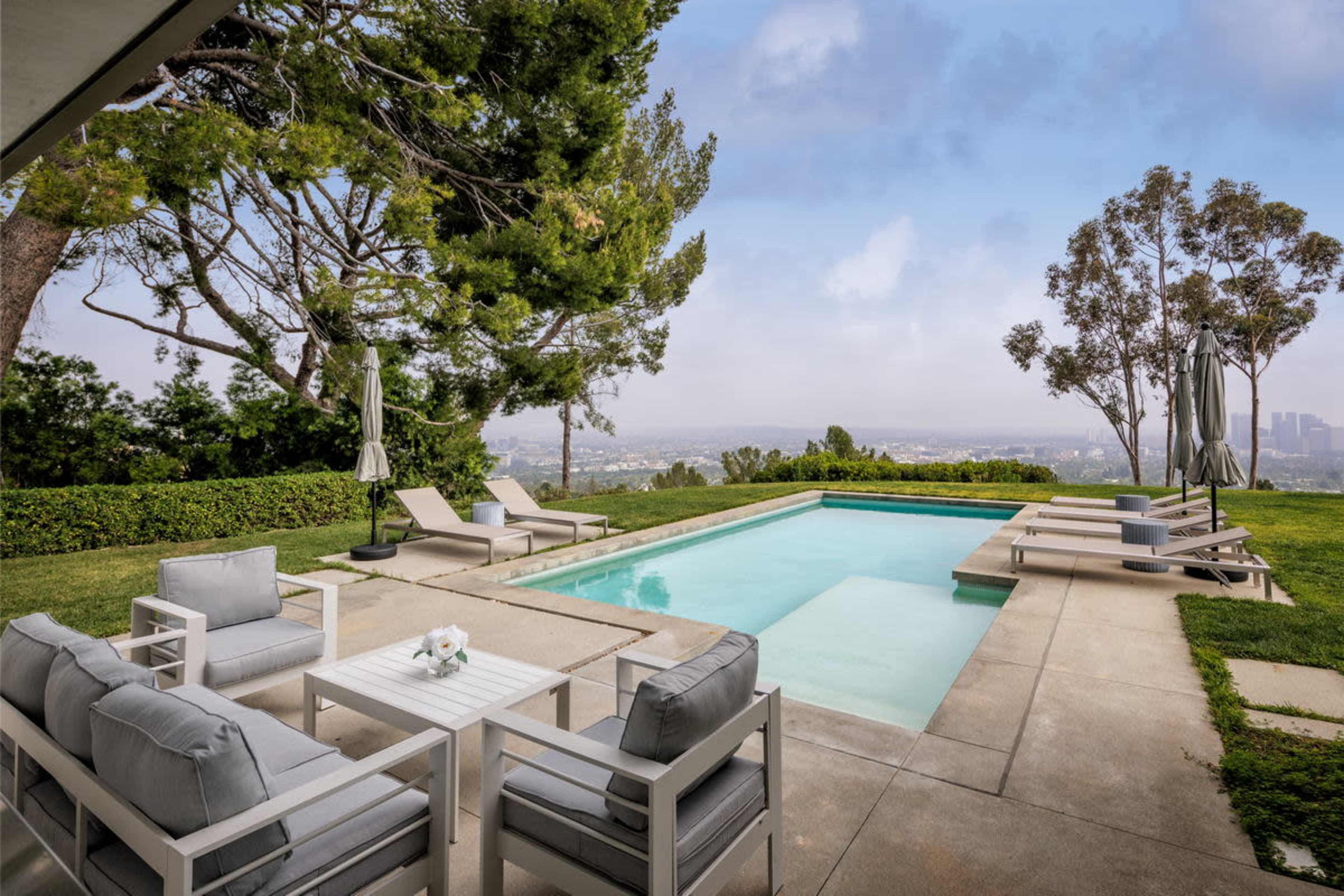 A modern outdoor space features a swimming pool, lounge chairs, and a seating area with a view of the skyline.