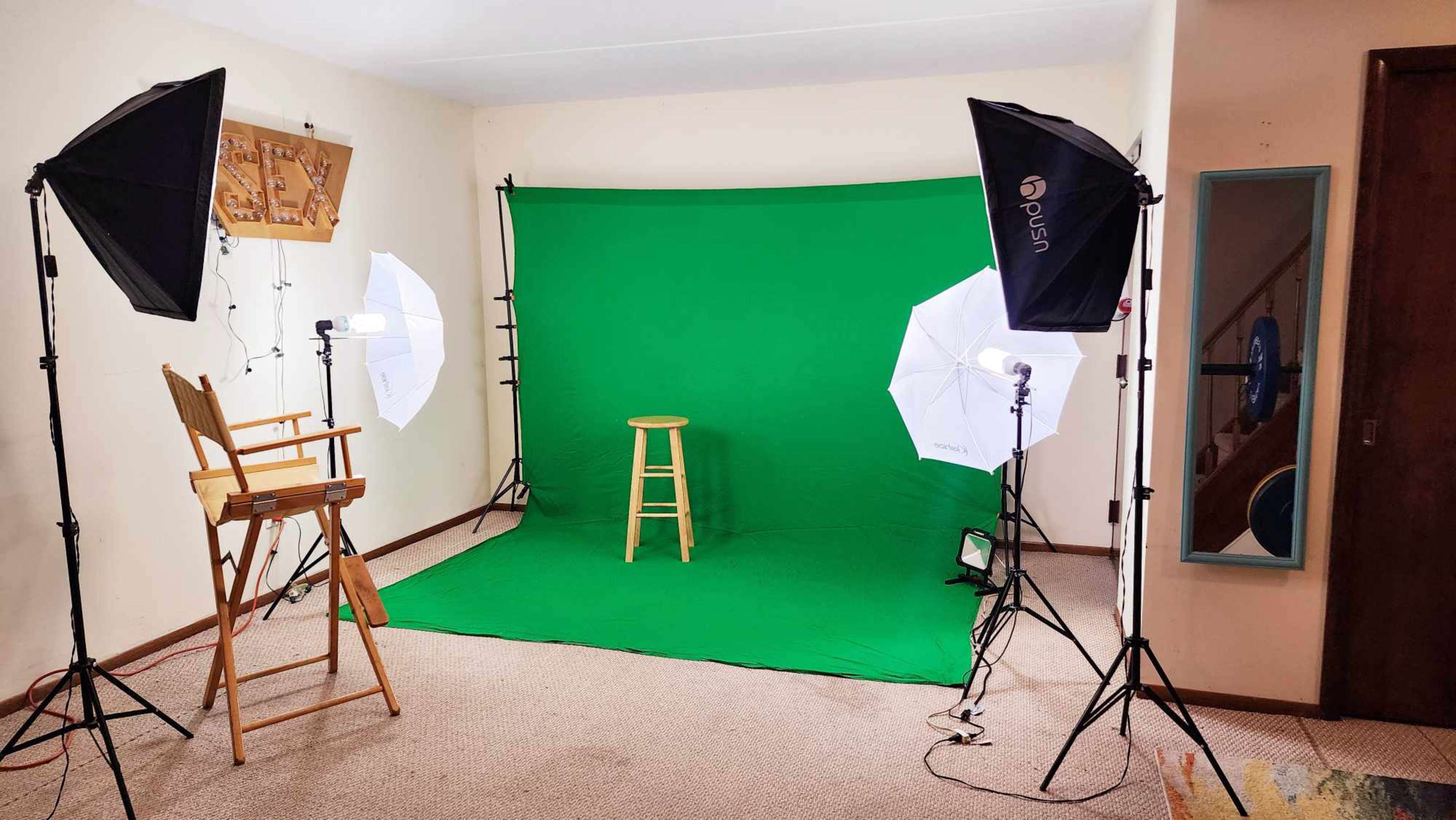The image shows a photography setup featuring a green backdrop, a wooden stool in the center, and multiple softbox lights positioned around the area.