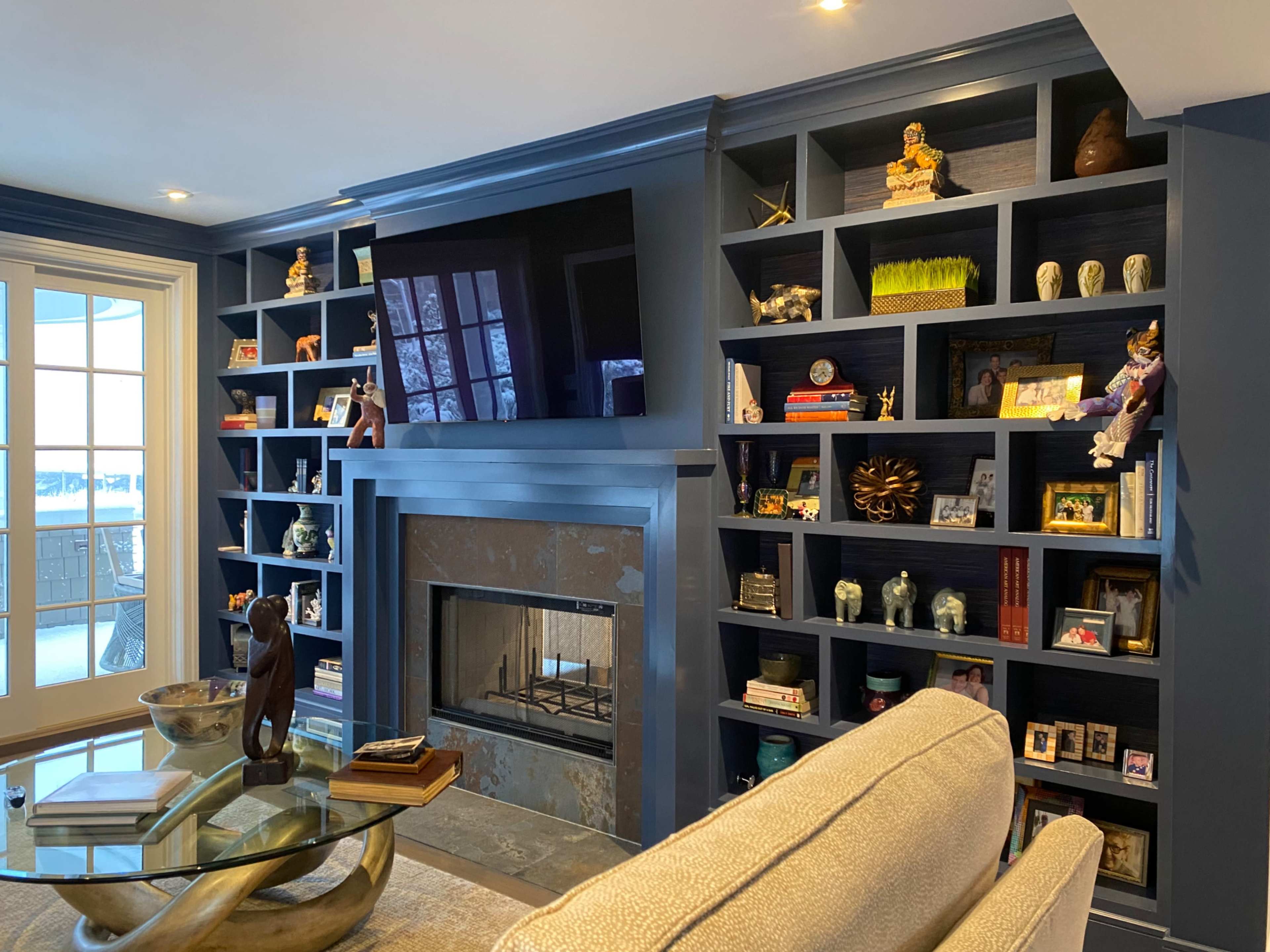 The image shows a modern living room with a blue wall featuring built-in shelves filled with decorative items and a fireplace beneath a mounted television.