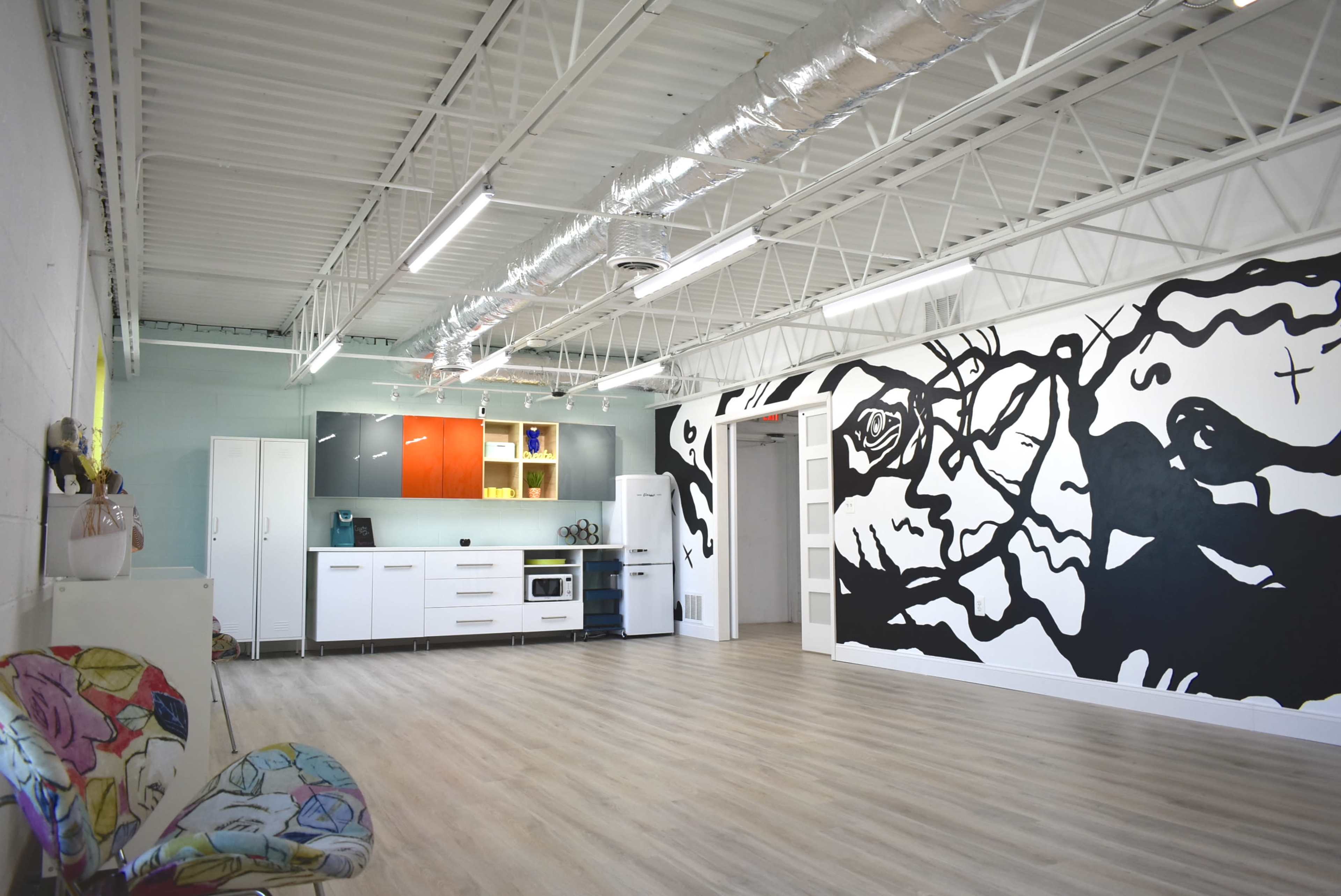 A spacious interior with a kitchenette featuring red and white cabinets and a large black and white mural on the wall.