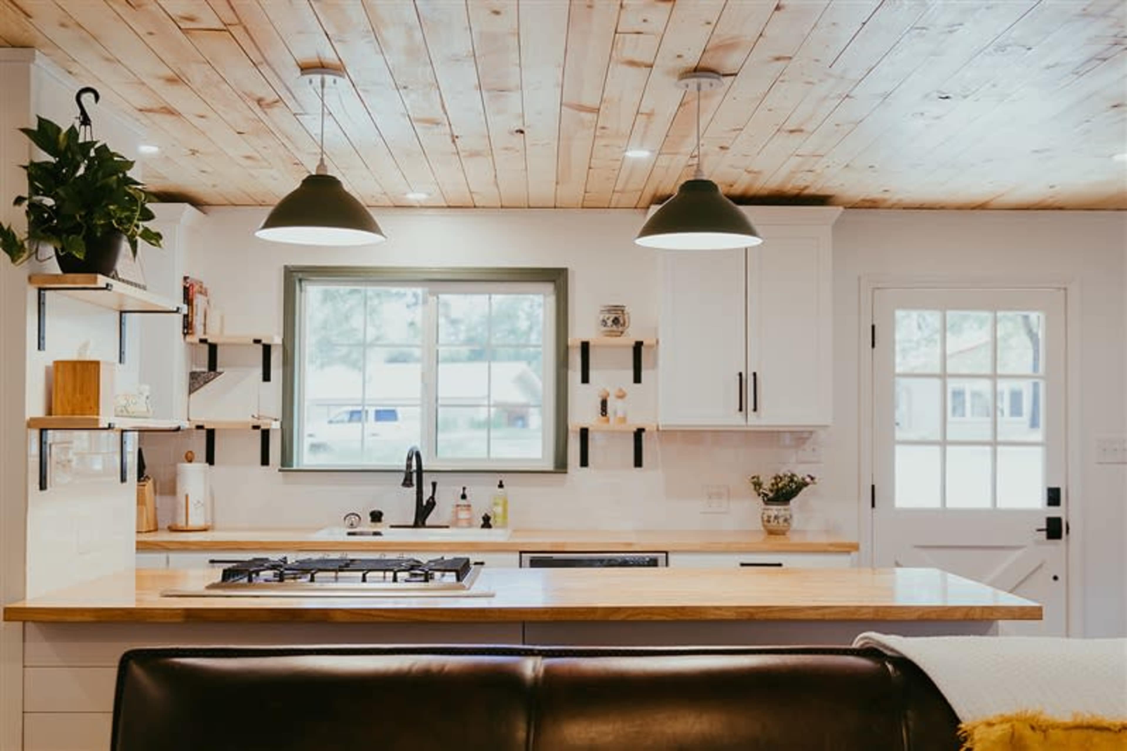 A modern kitchen features a central island with a gas stove, white cabinetry, and a large window above the sink.