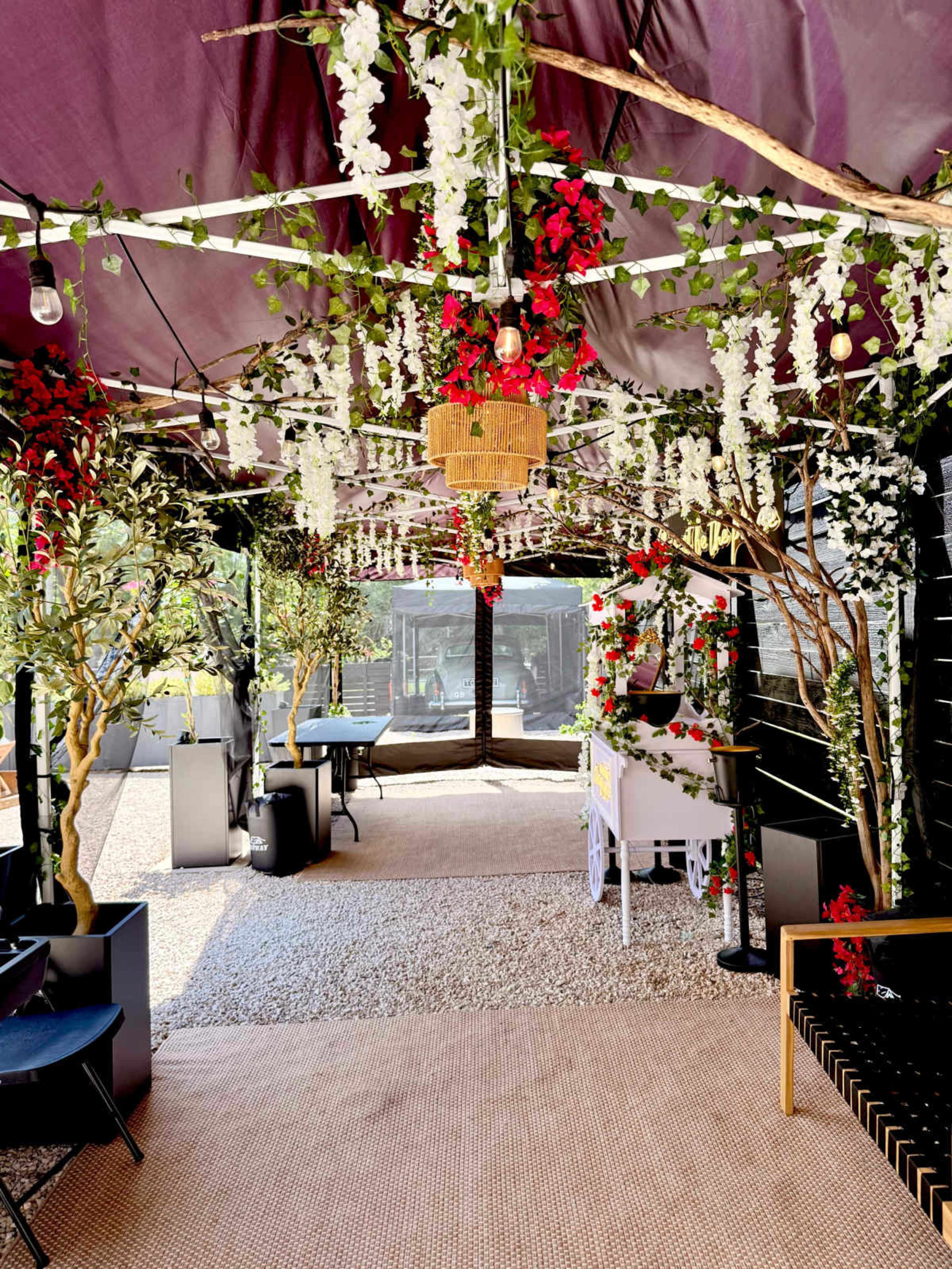 A decorative outdoor space is adorned with hanging flowers, string lights, and potted trees, creating an inviting atmosphere.
