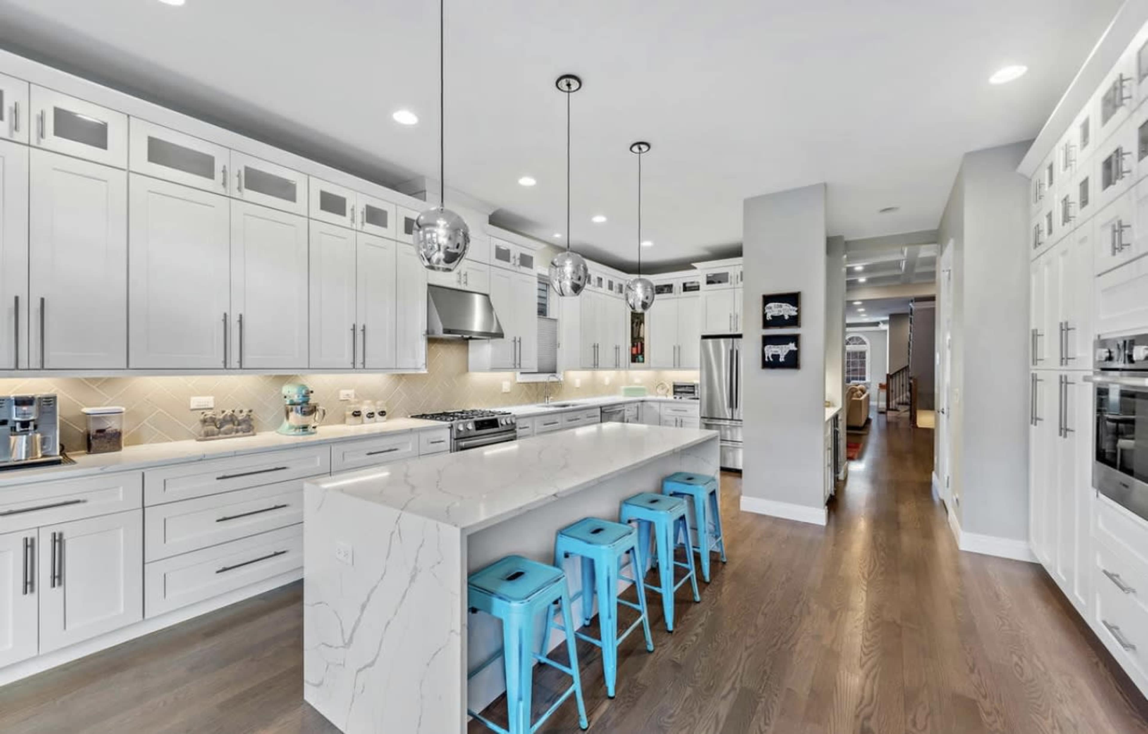 The kitchen features white cabinetry, a large island with a marble countertop, and turquoise bar stools.
