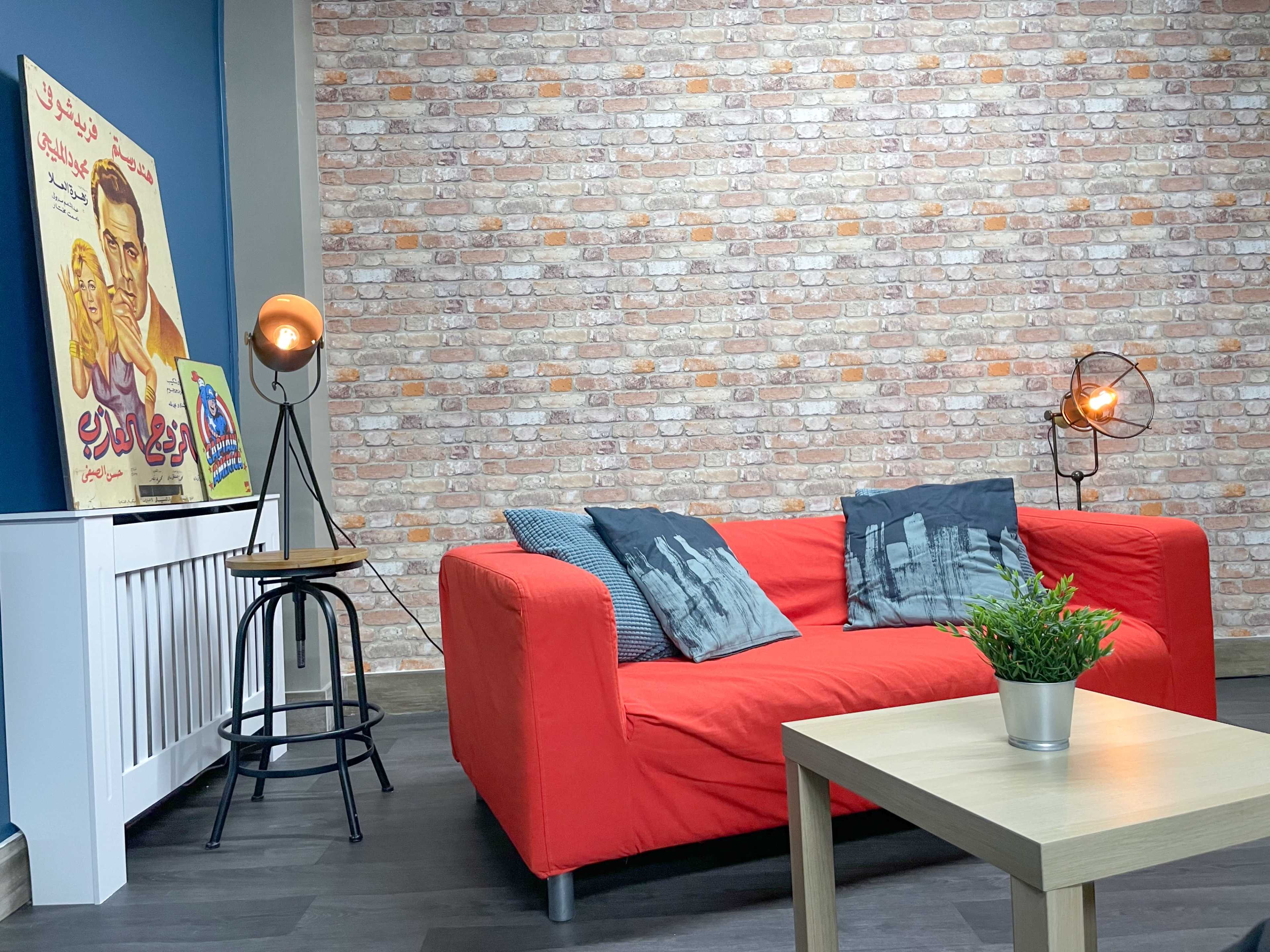 A modern living room with a red sofa, a small wooden table, and a vintage movie poster on the wall, set against a brick-patterned background.