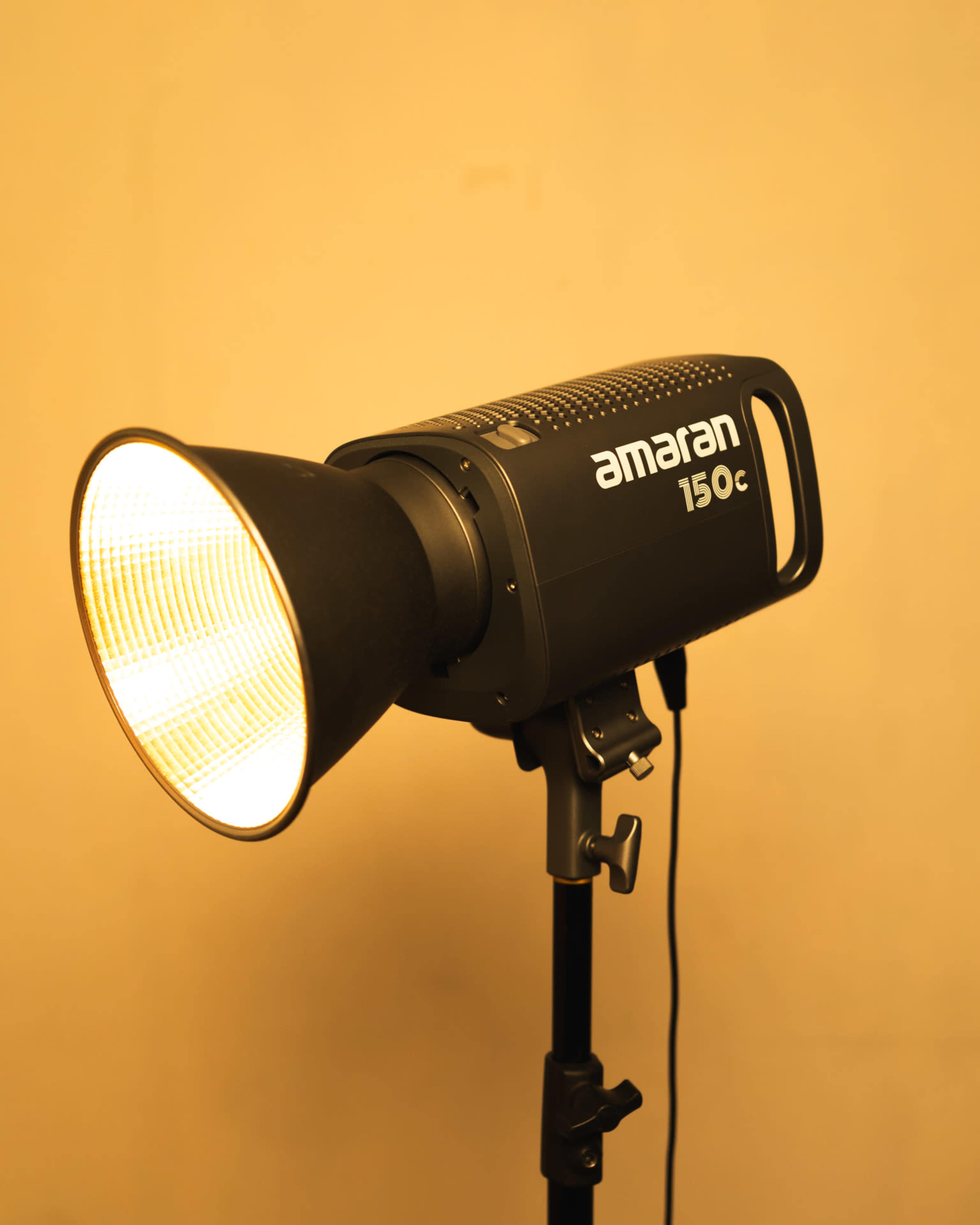 A studio light with a softbox attached stands on a tripod against a plain background.