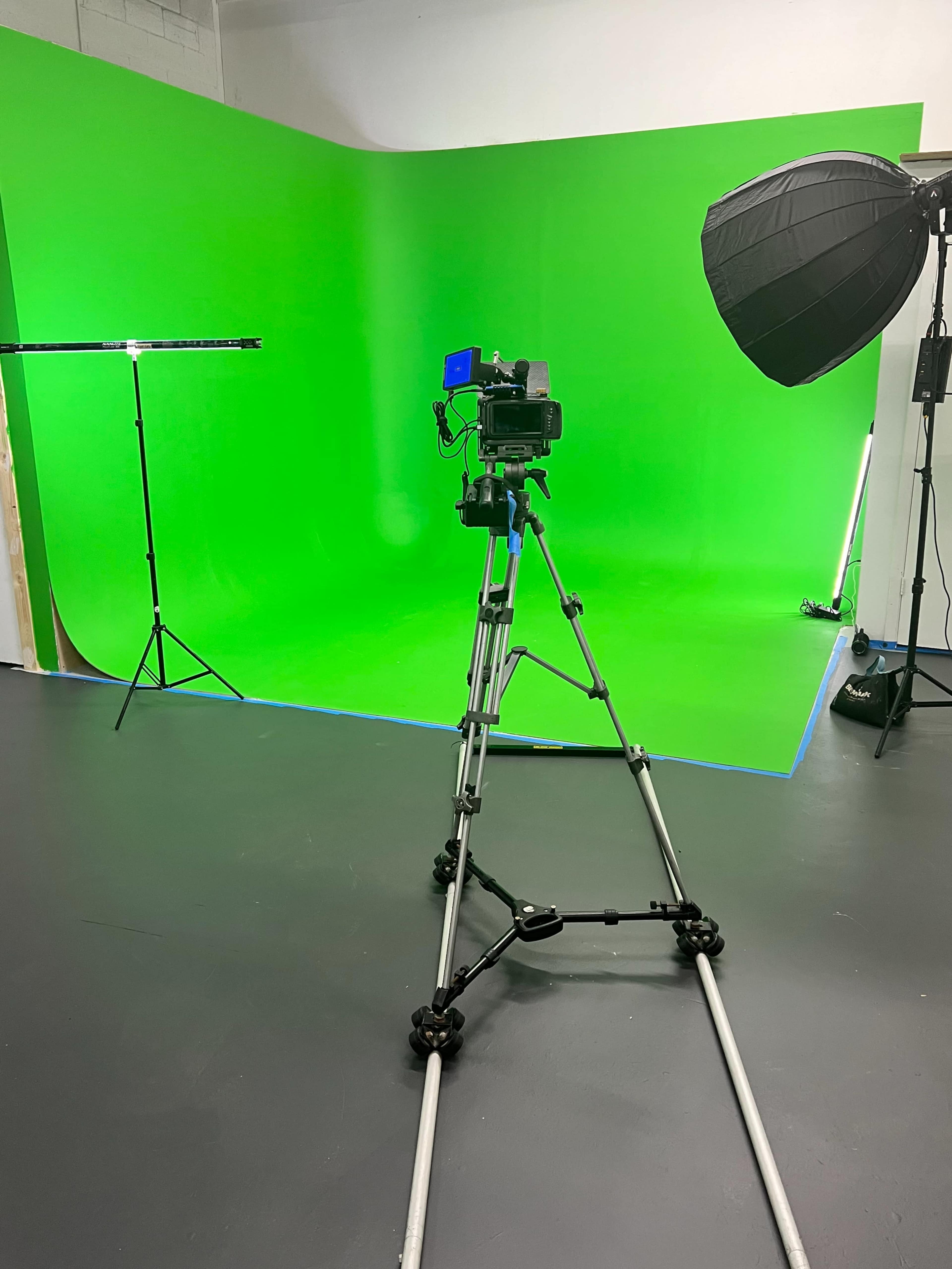 A camera on a tripod is positioned in front of a green screen in a studio setting.