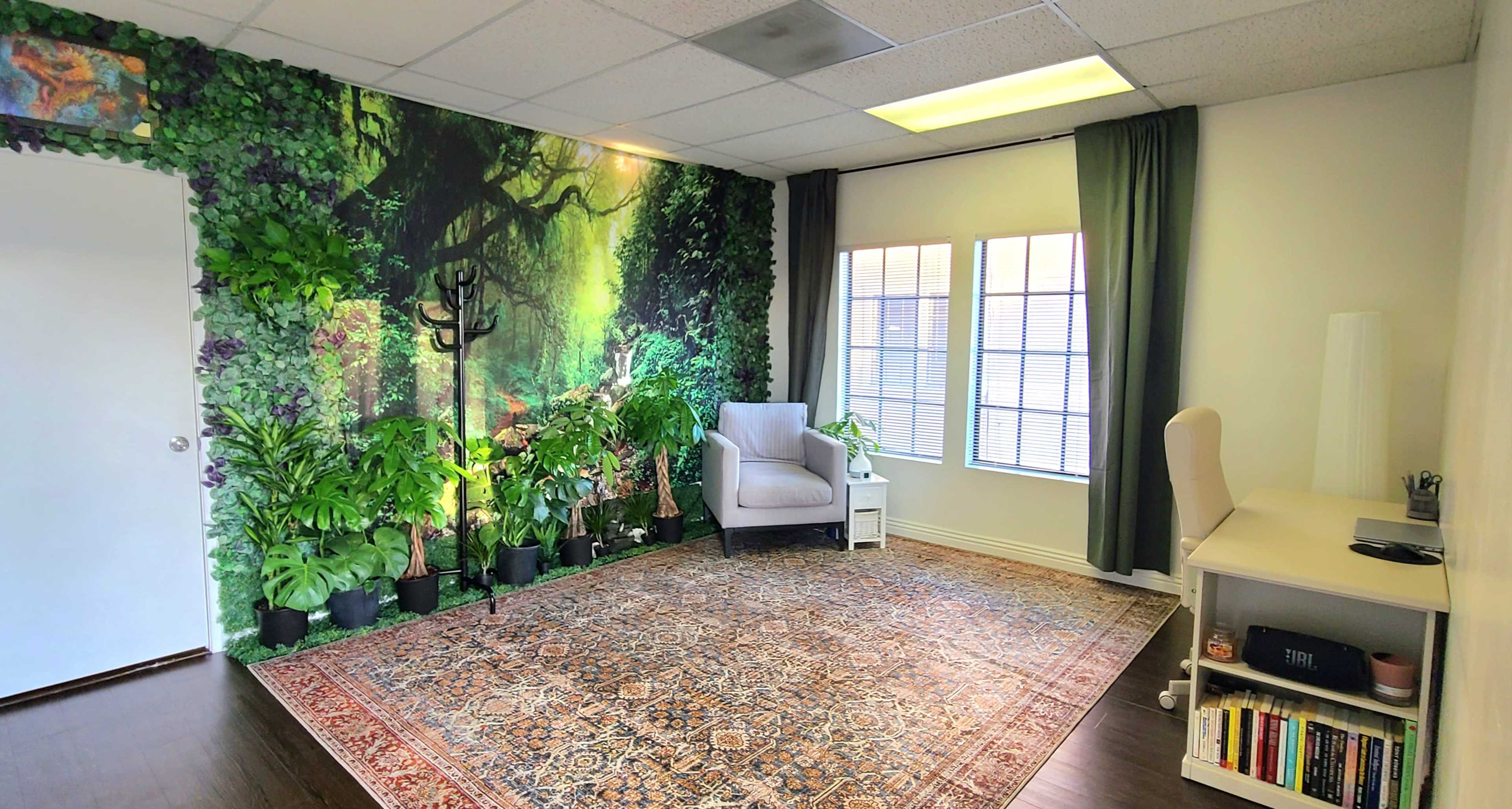 The room features a wall mural of a forest, surrounded by various potted plants, a cozy chair, and a desk against a window.