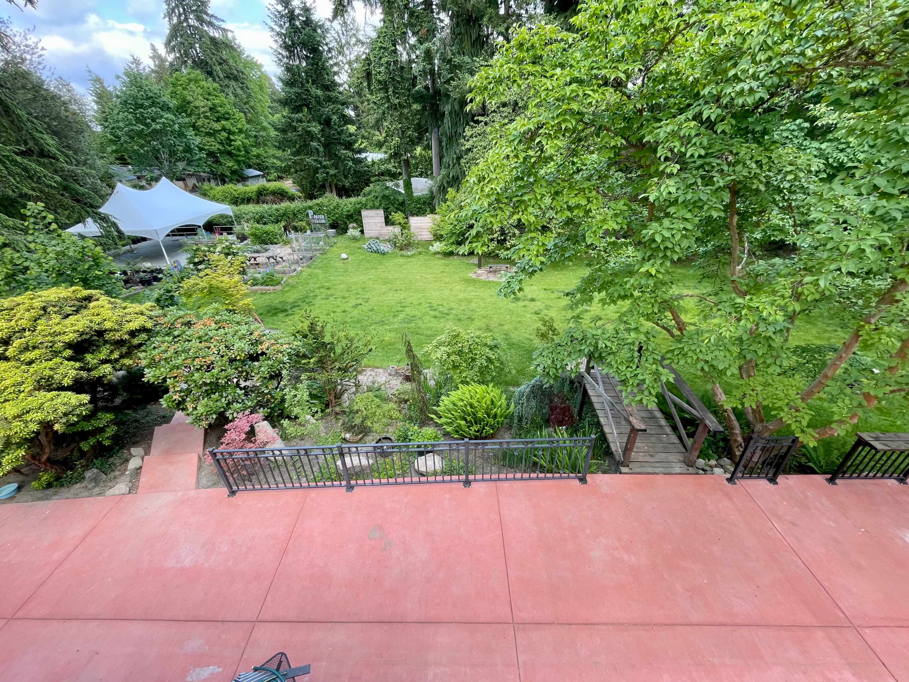 A spacious backyard features a manicured lawn, garden beds, and a stone pathway leading through lush greenery.