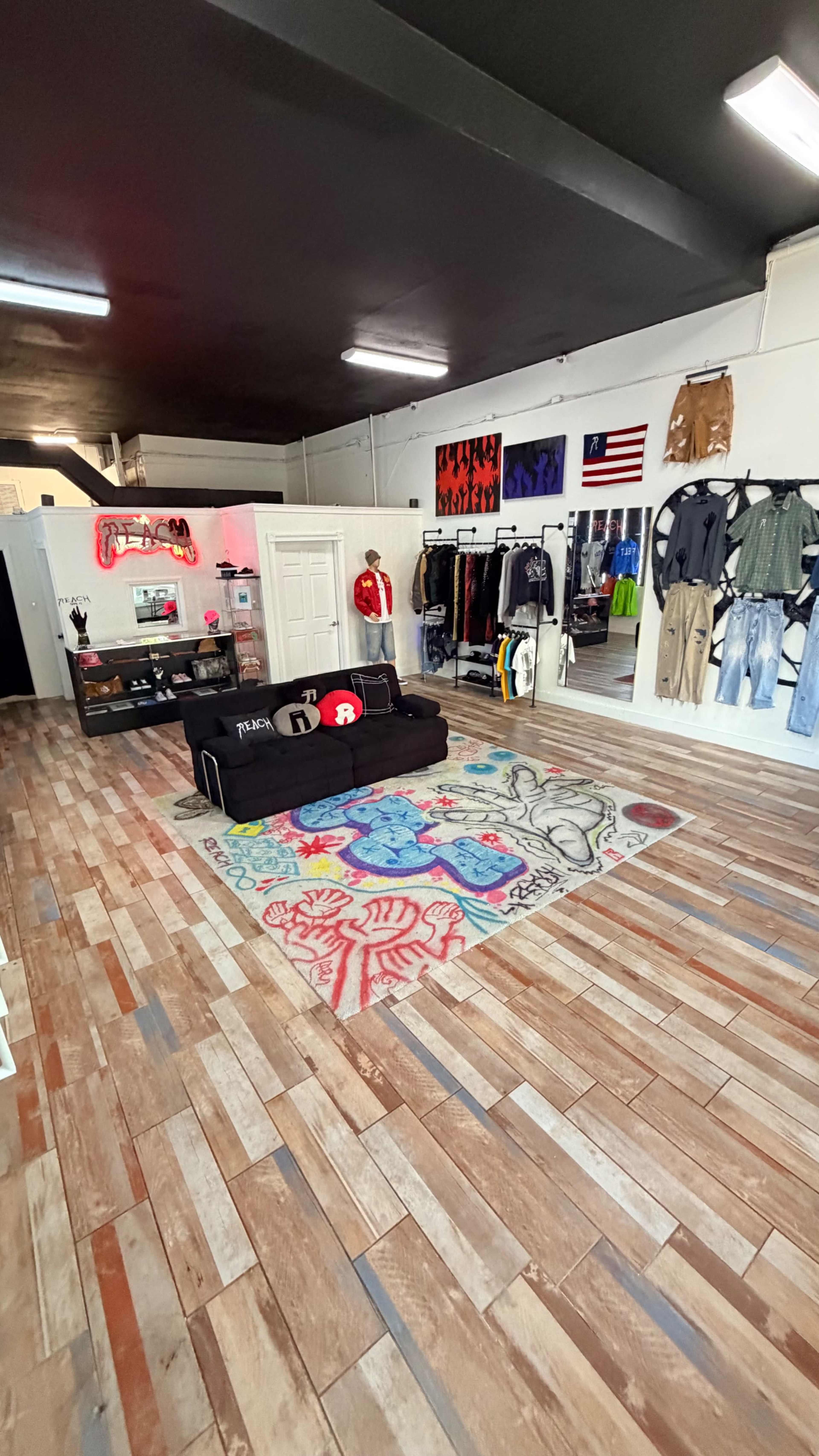 The image shows a trendy retail space with a colorful rug, clothing racks, and a display area featuring a couch and various apparel items.