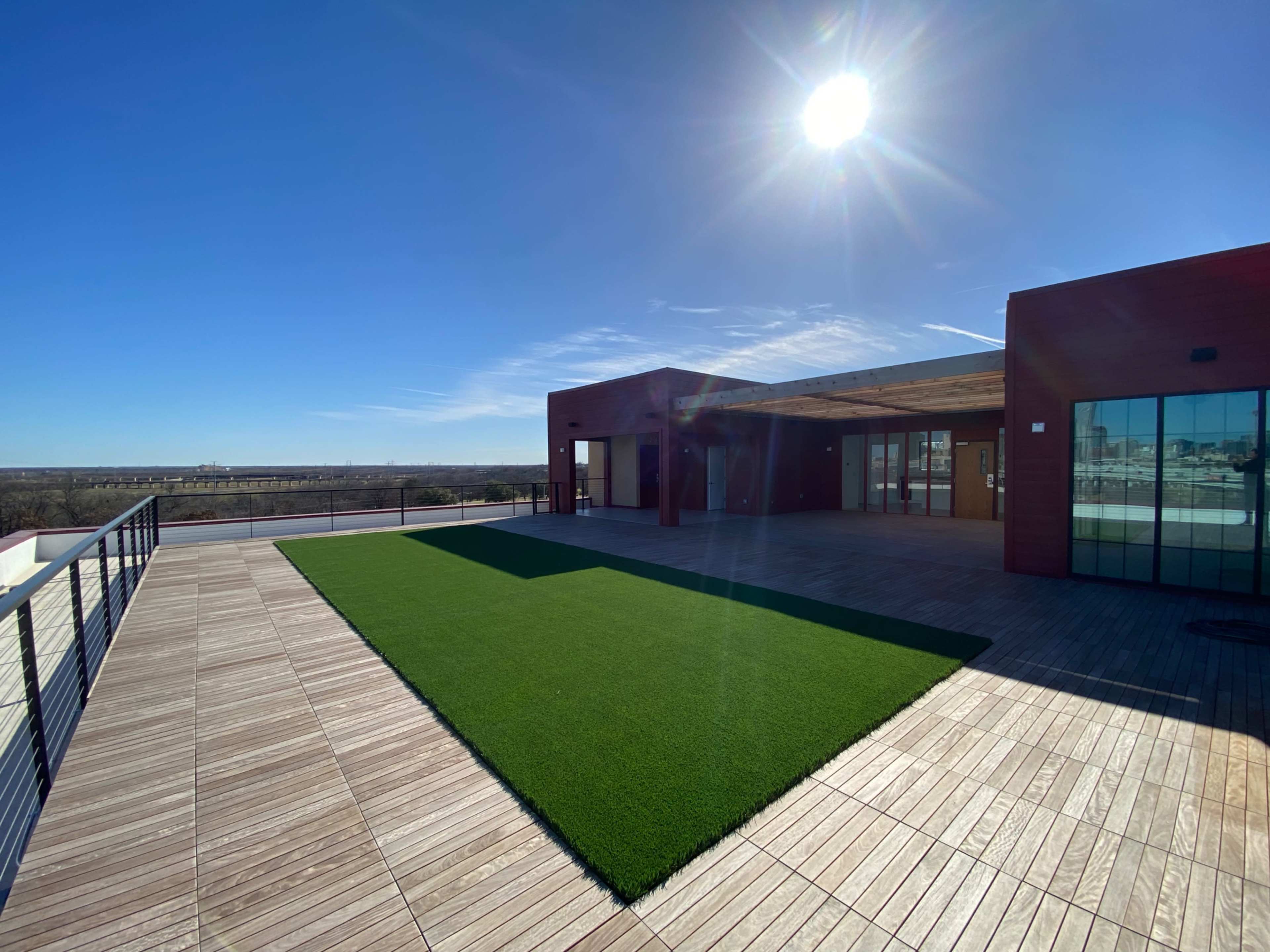 A spacious rooftop terrace features wooden decking and a section of artificial grass under a clear blue sky.