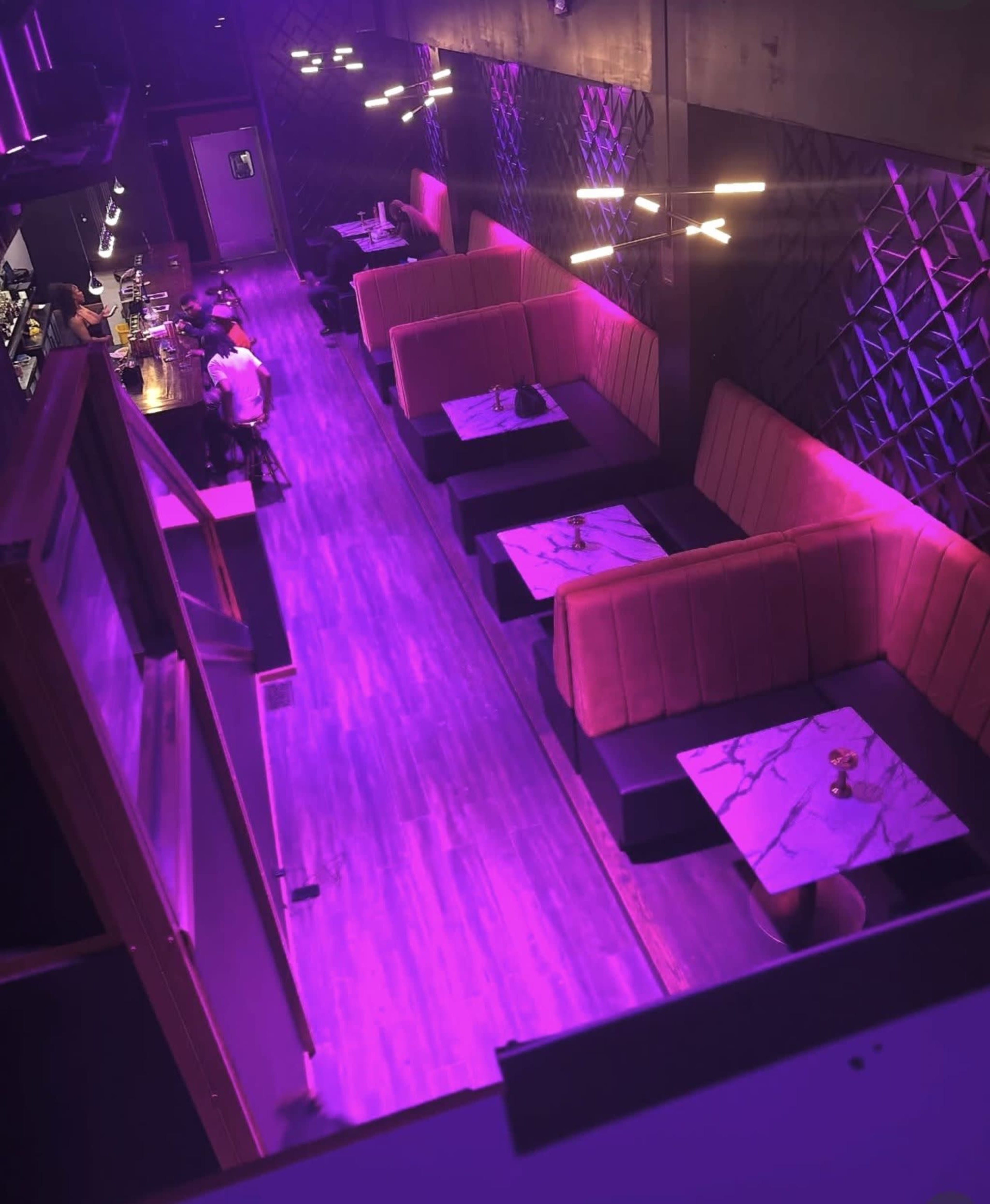 The image shows a long, dimly lit lounge with purple lighting, featuring several booth seating areas with marble-topped tables.