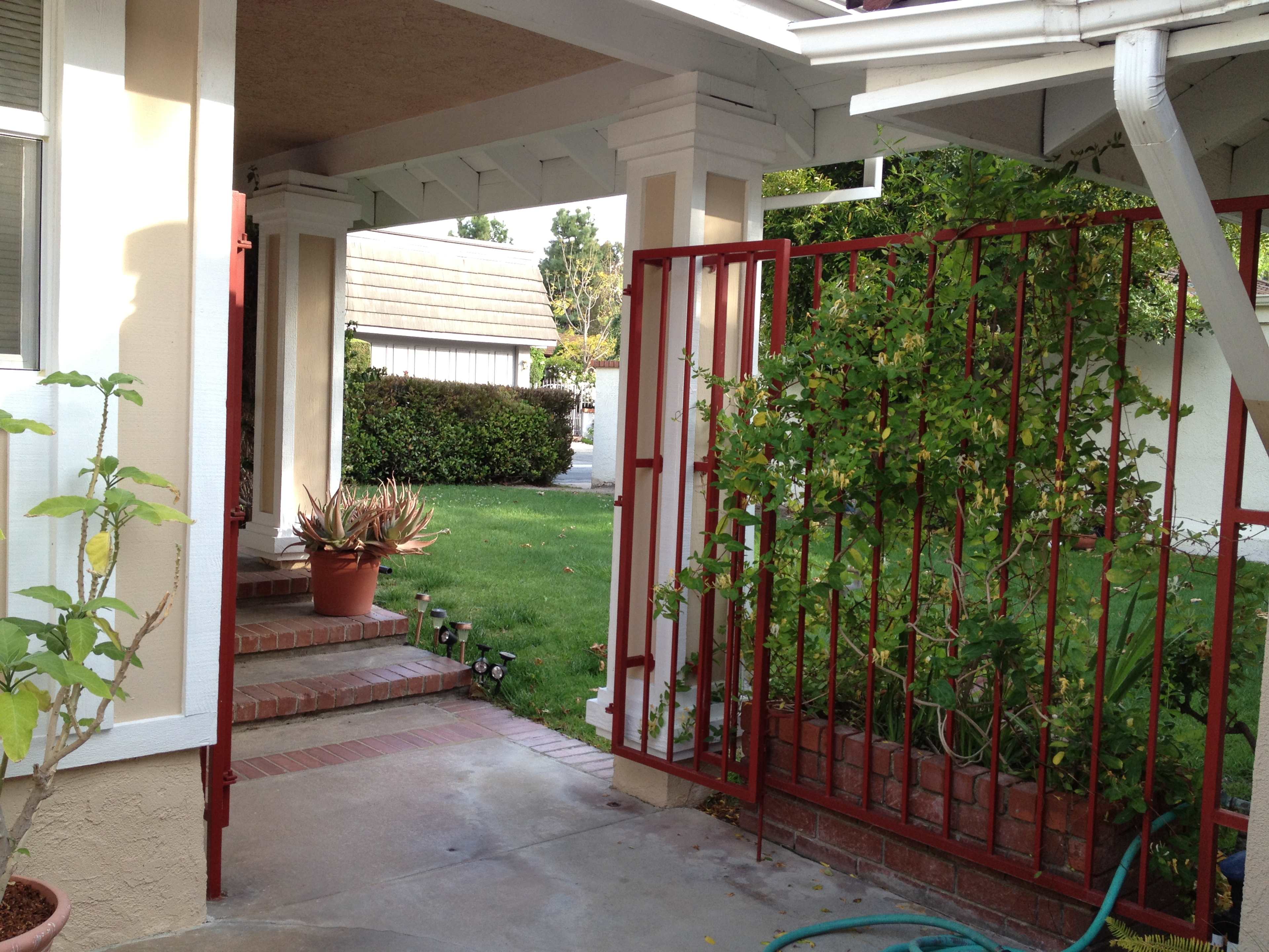 A pathway leading through a gated entryway to a grassy area surrounded by plants and shrubs.
