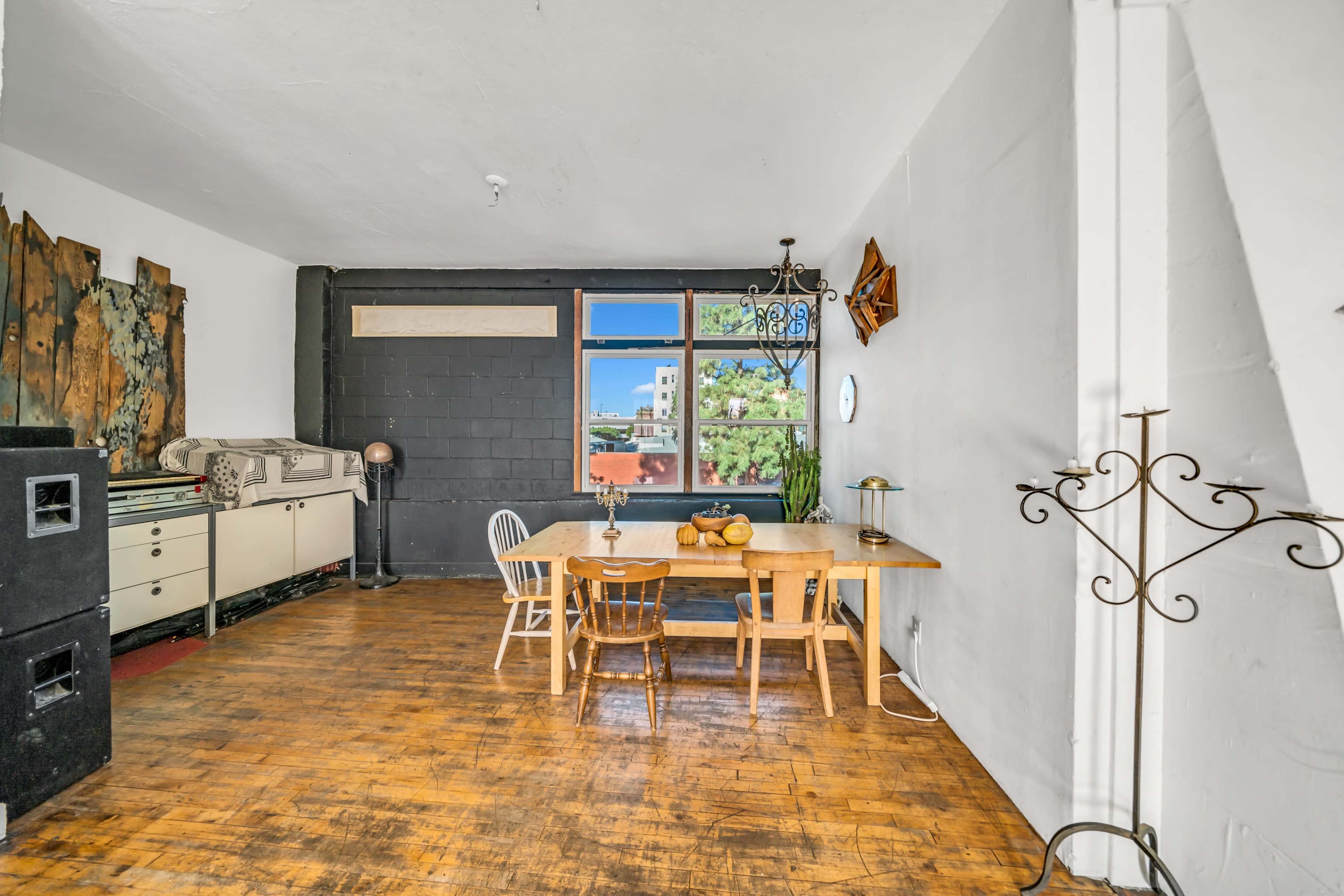 The image shows a spacious interior with a dining area featuring a wooden table and chairs, large windows allowing natural light, and various decorative elements on the walls.